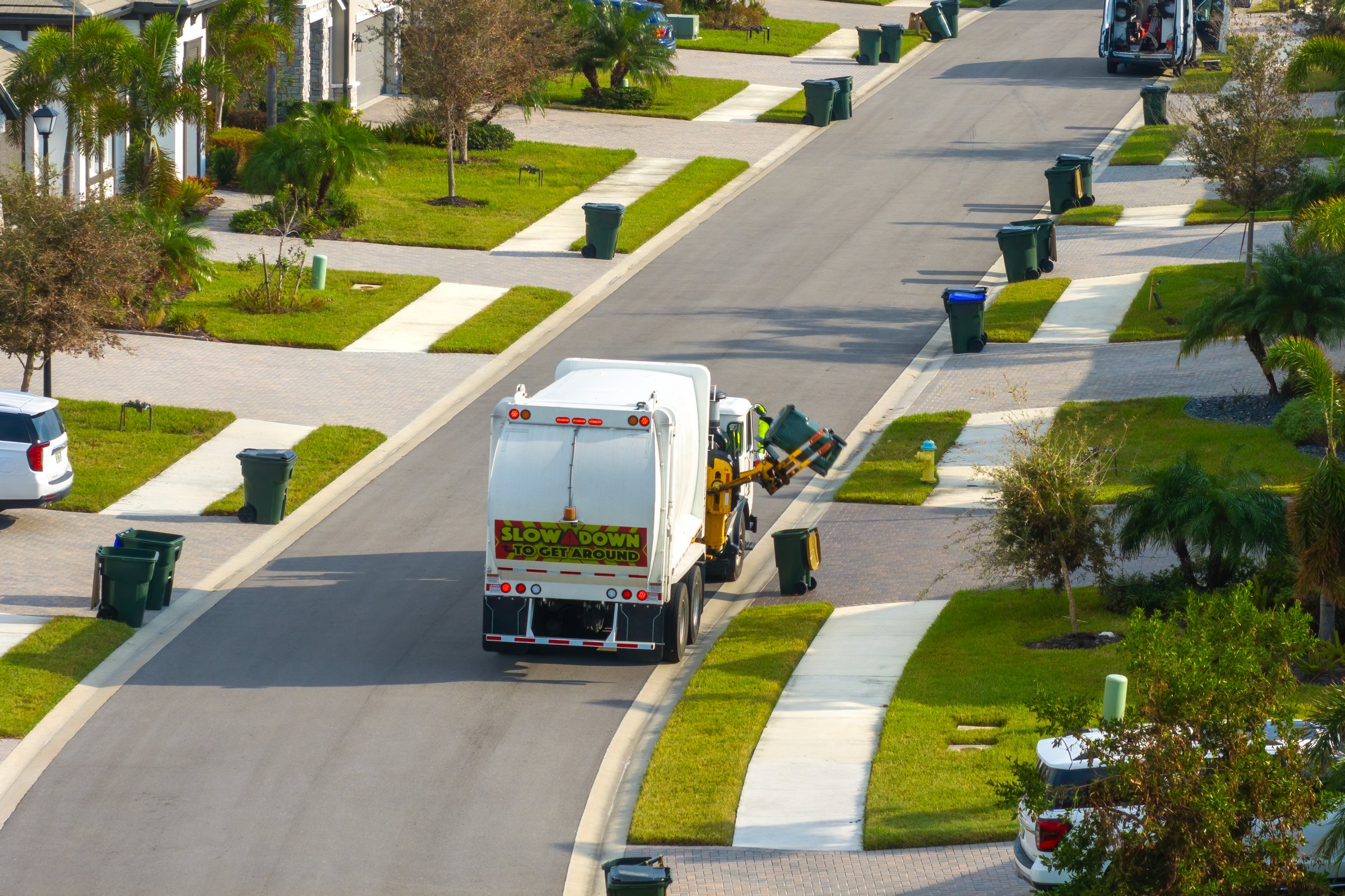 Garbage truck picking up trash bins on suburban street side.