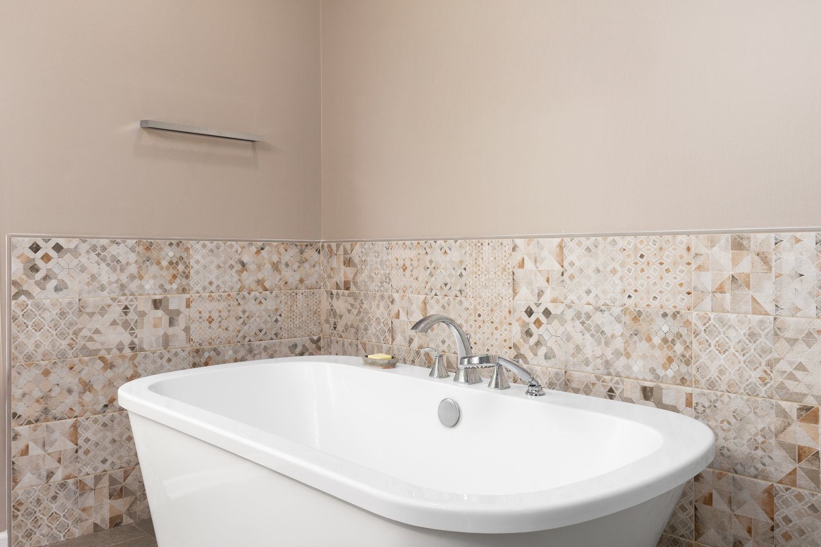 A freestanding bathtub detail with a chrome faucet surrounded by brown walls and a brown square pattern tile with geometric shapes.