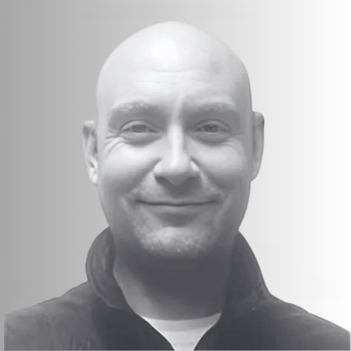 A grayscale headshot of a smiling bald man wearing a dark jacket against a plain background.