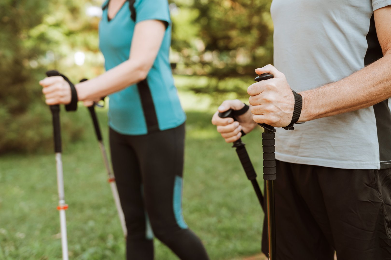 Two people are holding trekking poles while exercising outdoors. They are enjoying their retirement in a peaceful environment