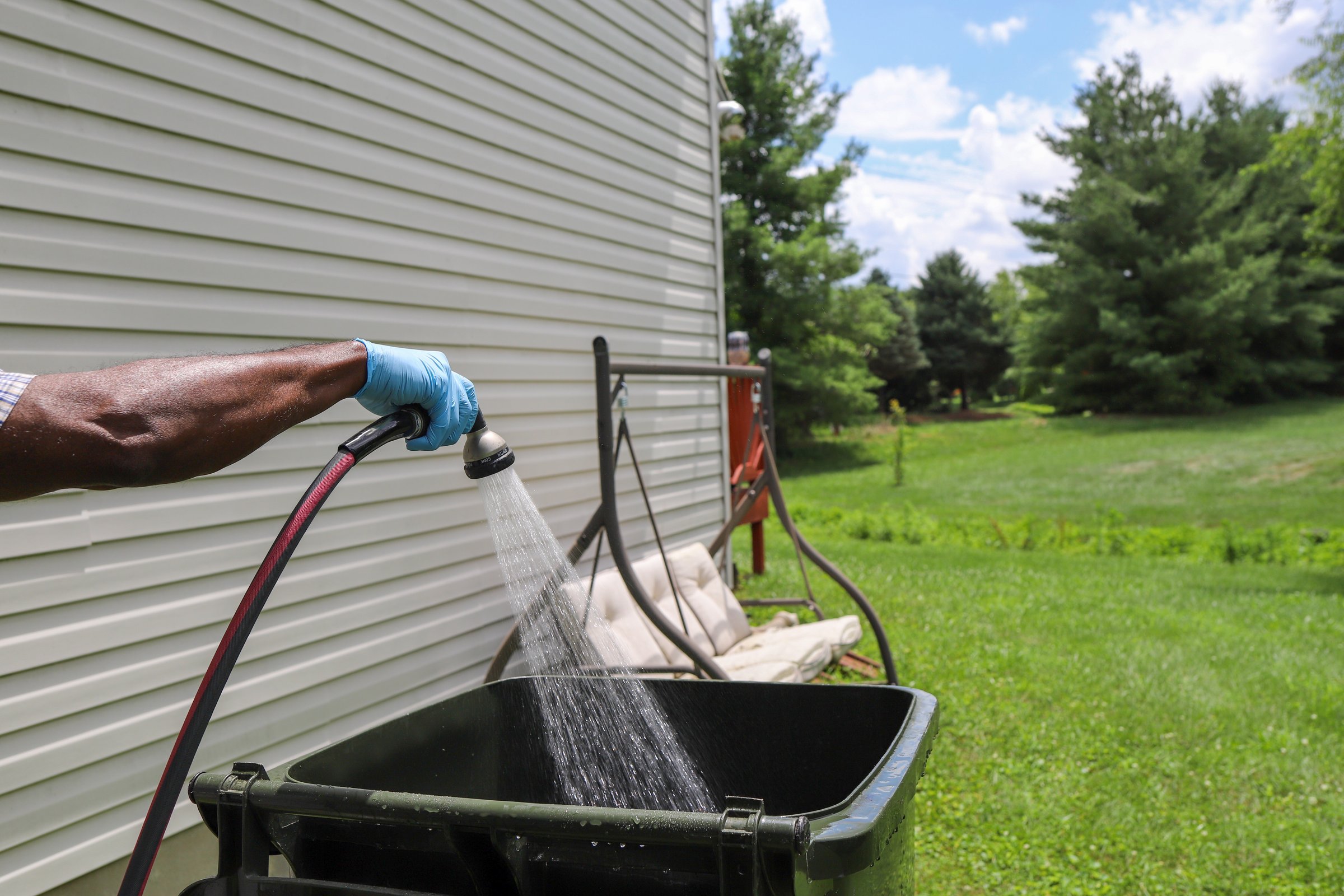 A black African-American man cleaning and spraying out a garbage can