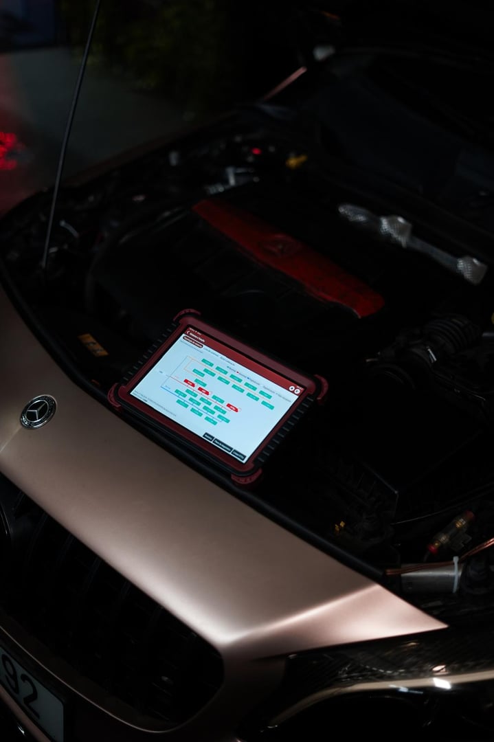 A mechanic using a laptop on a car engine for diagnostics in a garage. Highlights the use of technology in modern vehicle maintenance and repair.