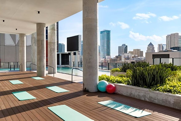 Outdoor yoga area with mats, exercise balls, and views of the city skyline and pool.
