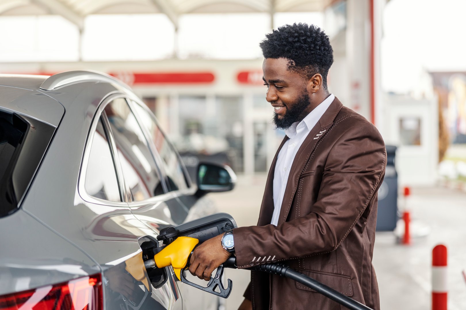Happy african american man standing at gas station and filling up car tank with gasoline.