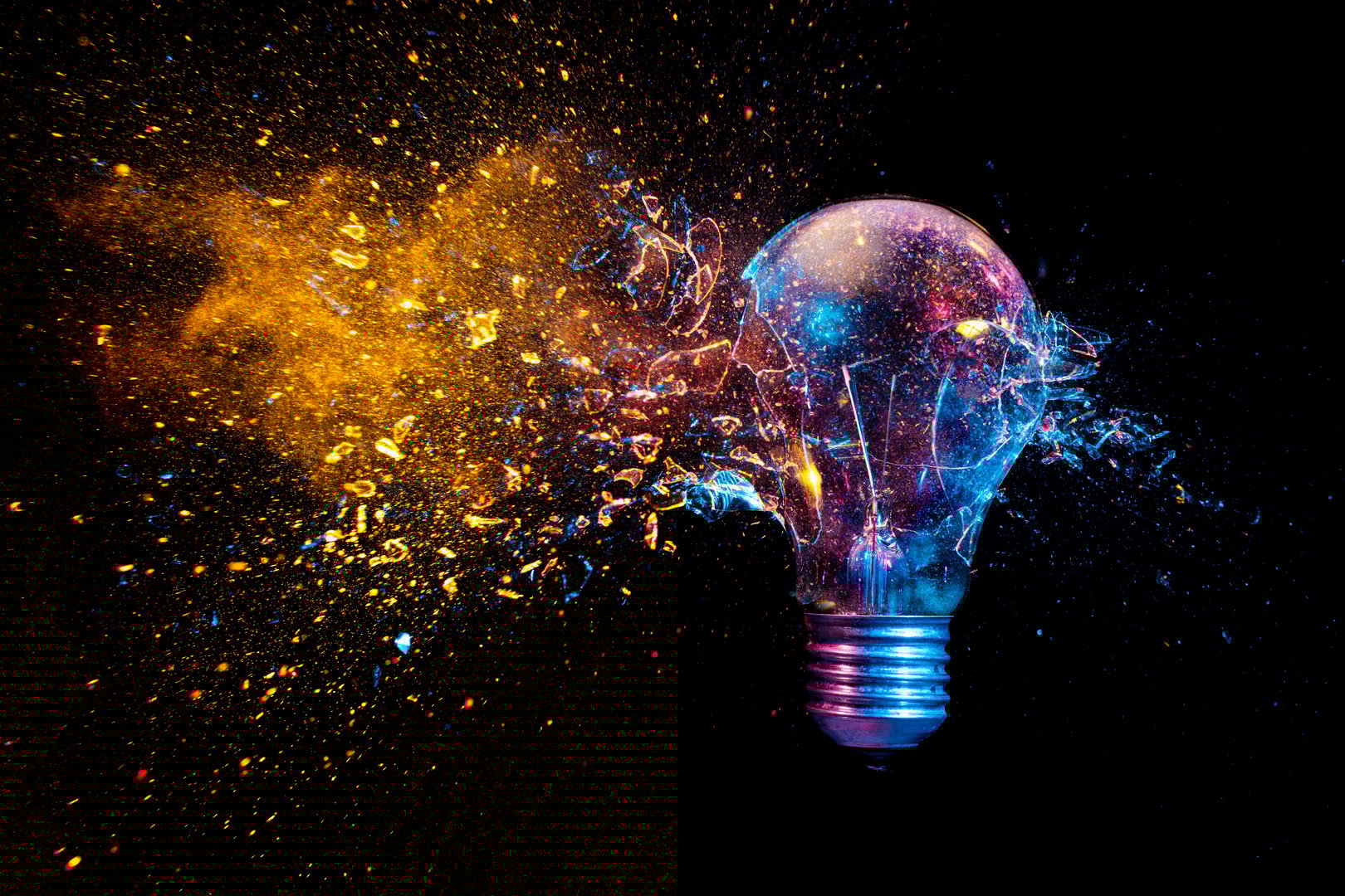 explosion of a traditional electric bulb. shot taken in high speed, at the exact moment of impact. Colored lights and black background. concept of creativity and fragility.