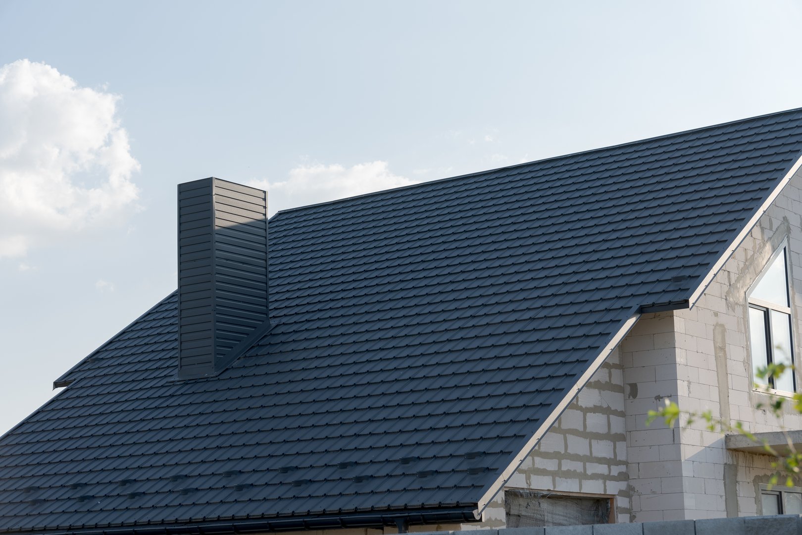 Crafted with care, the sleek slate roof crowns a newly built home, reflecting modern architecture against a backdrop of blue skies and soft clouds.