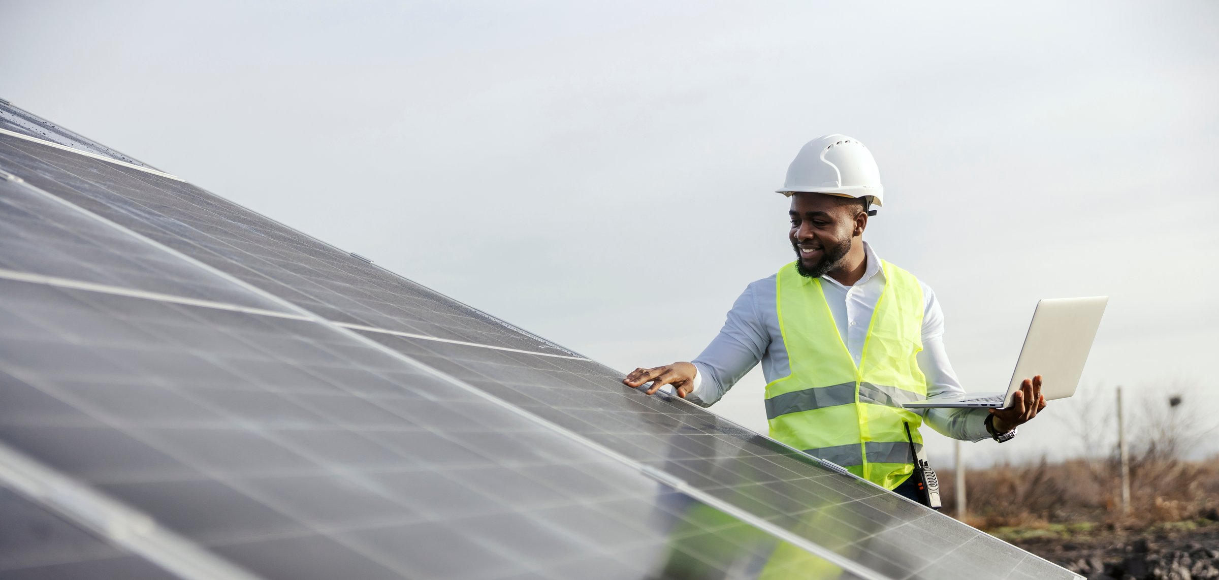 Interracial inspector with tablet in hands standing at solar power plant and examining solar panels.
