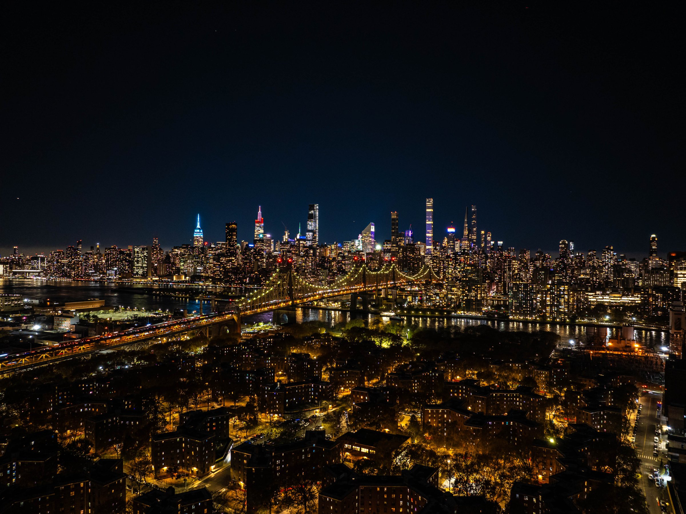 Illuminated Queensboro Bridge connecting Manhattan and Queens, part of the stunning New York City skyline glowing at night.