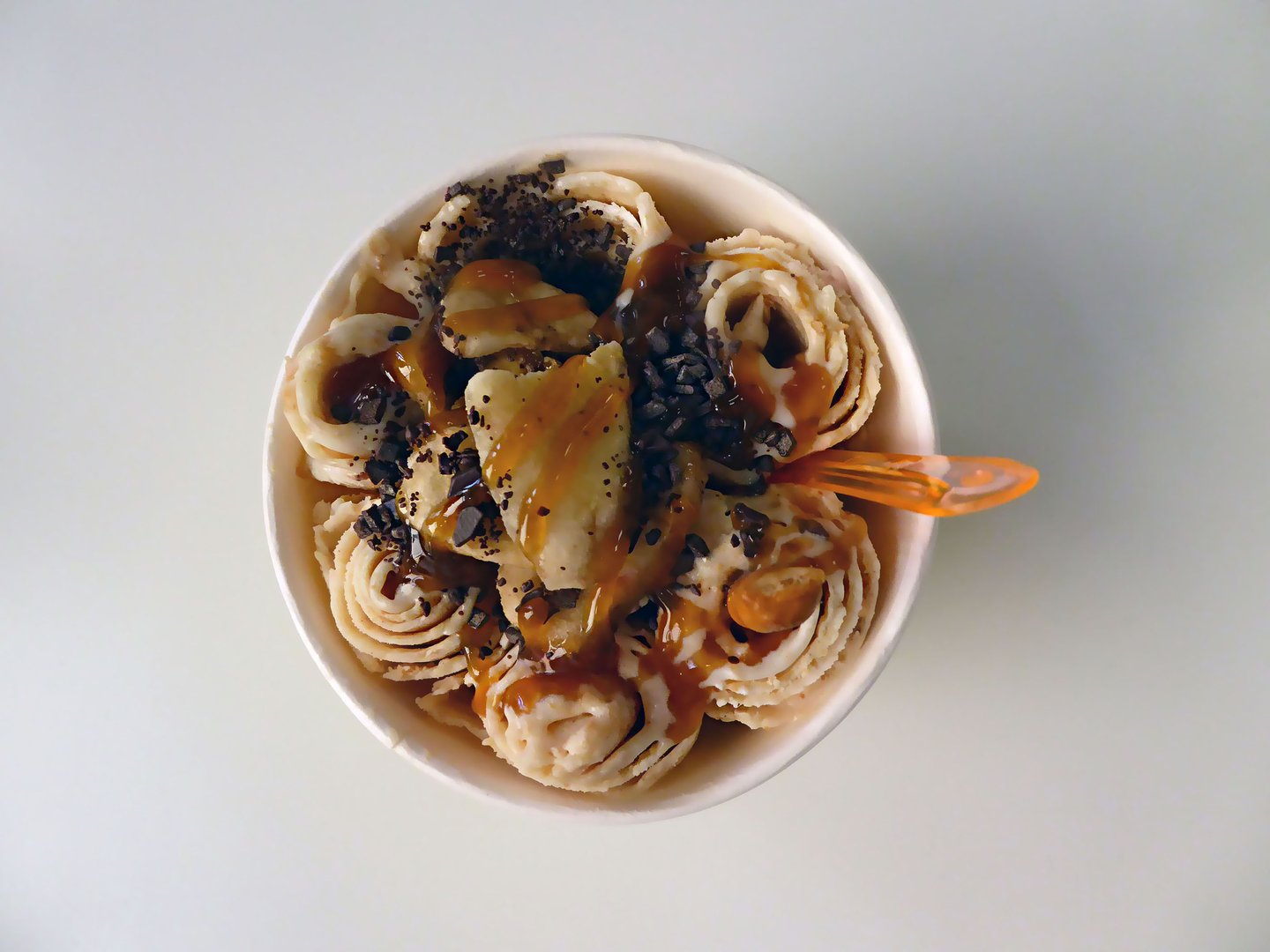 Bowl of rolls of ice cream with plastic spoon  top view