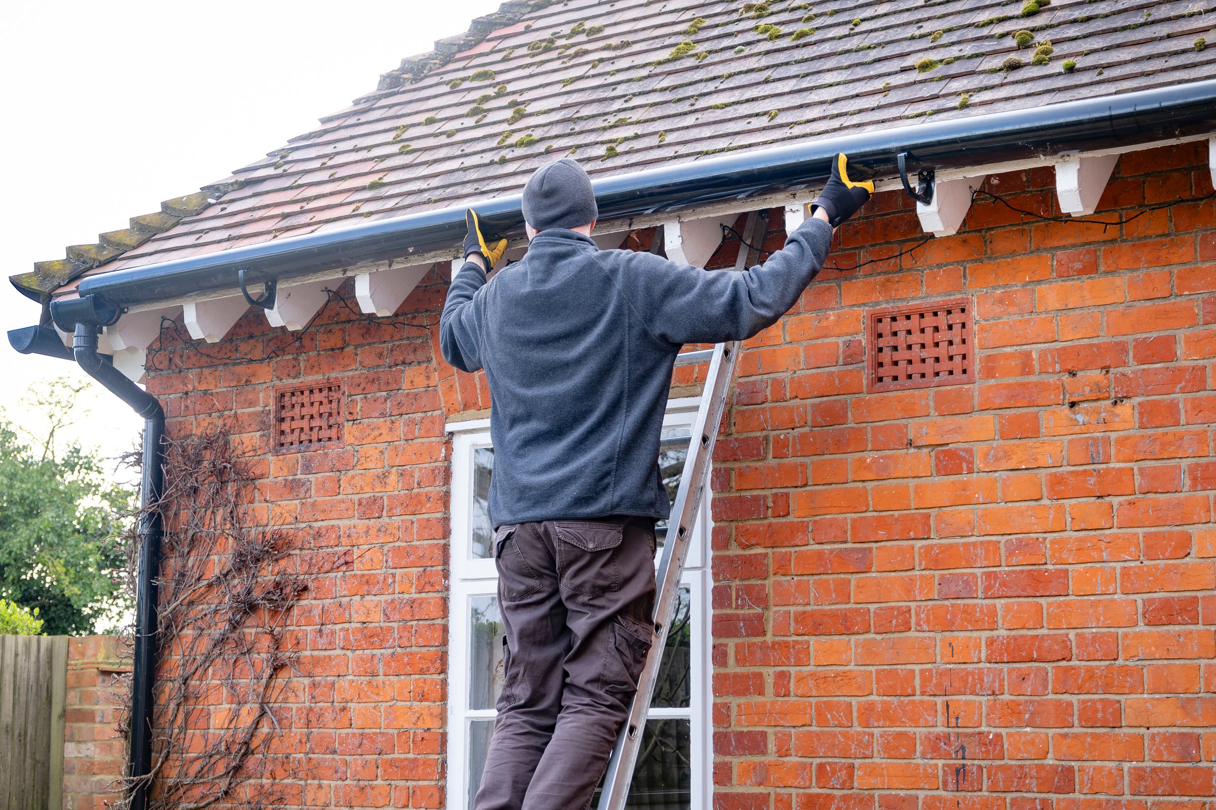 Man on a ladder fixing fitting a rain gutter on the eaves of a UK house