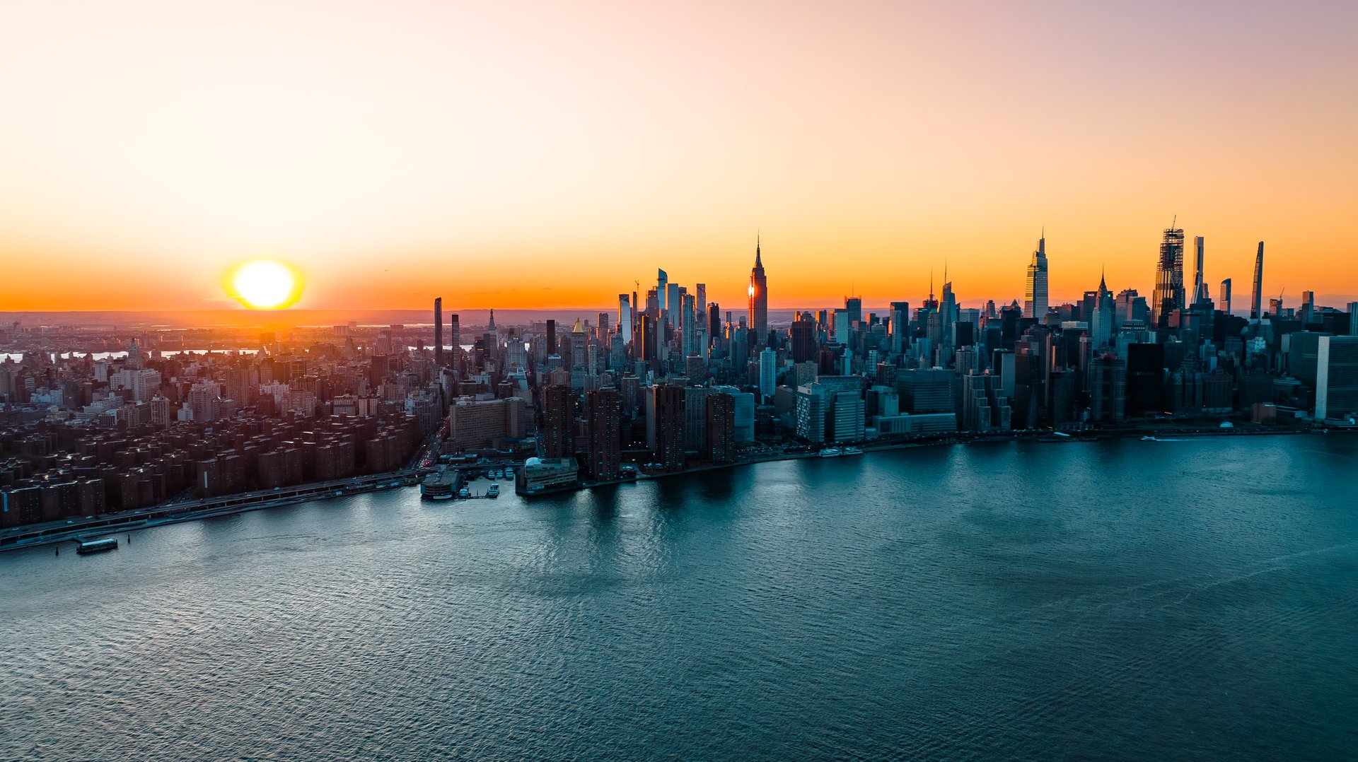 Orange light of setting sun illuminating the skyscrapers and high-rise buildings in New York scenery. Top view on the metropolis from above the East River..