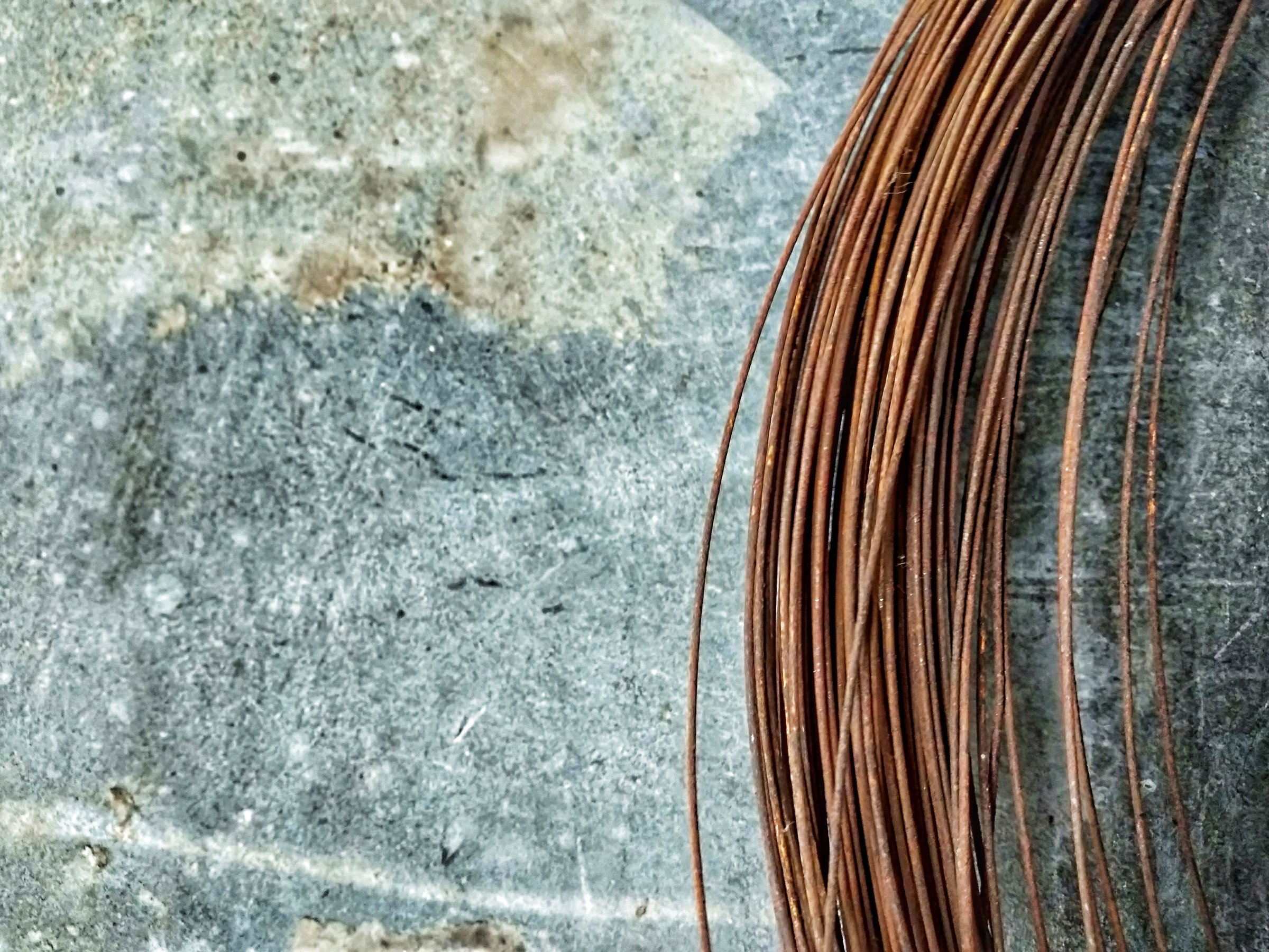 Object shot of a rusted coil of wire hanging from an age-textured wall, shot from a close-up.