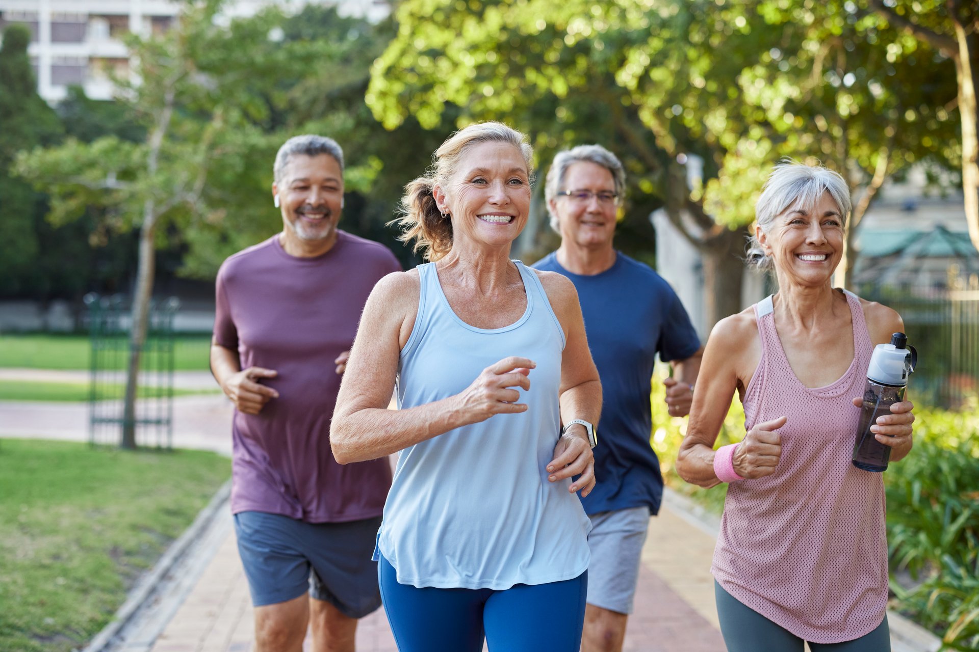 Group of happy older friends jogging in a city park. Fitness seniors running together outdoors while smiling. Mature multiethnic men and women enjoying a healthy morning workout.