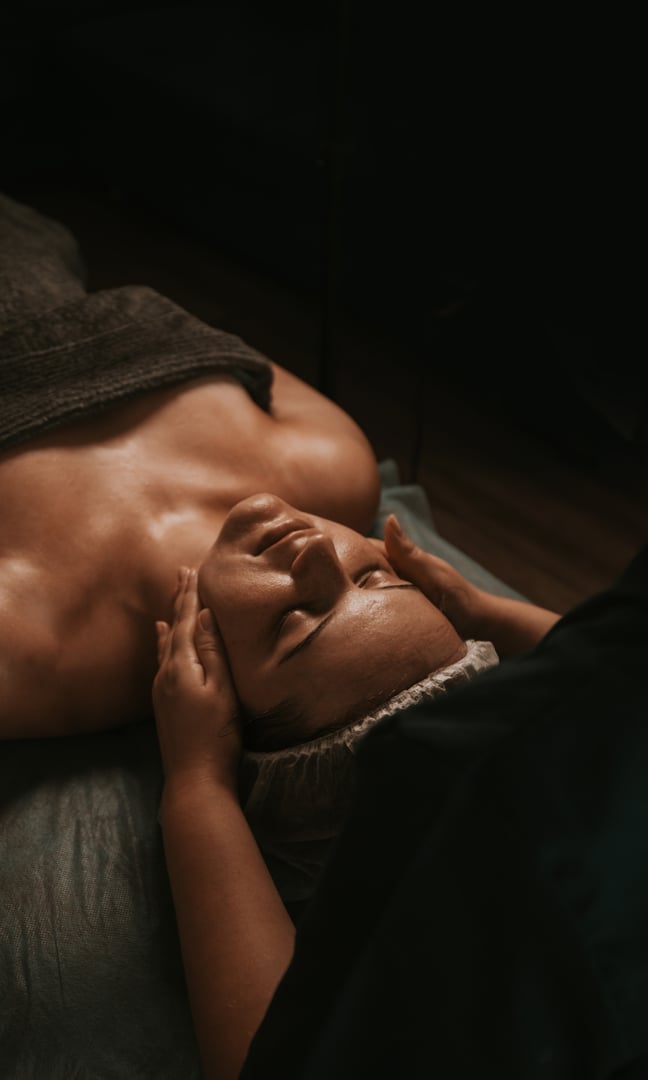 Woman receiving facial massage in dimly lit spa setting for relaxation and skincare therapy