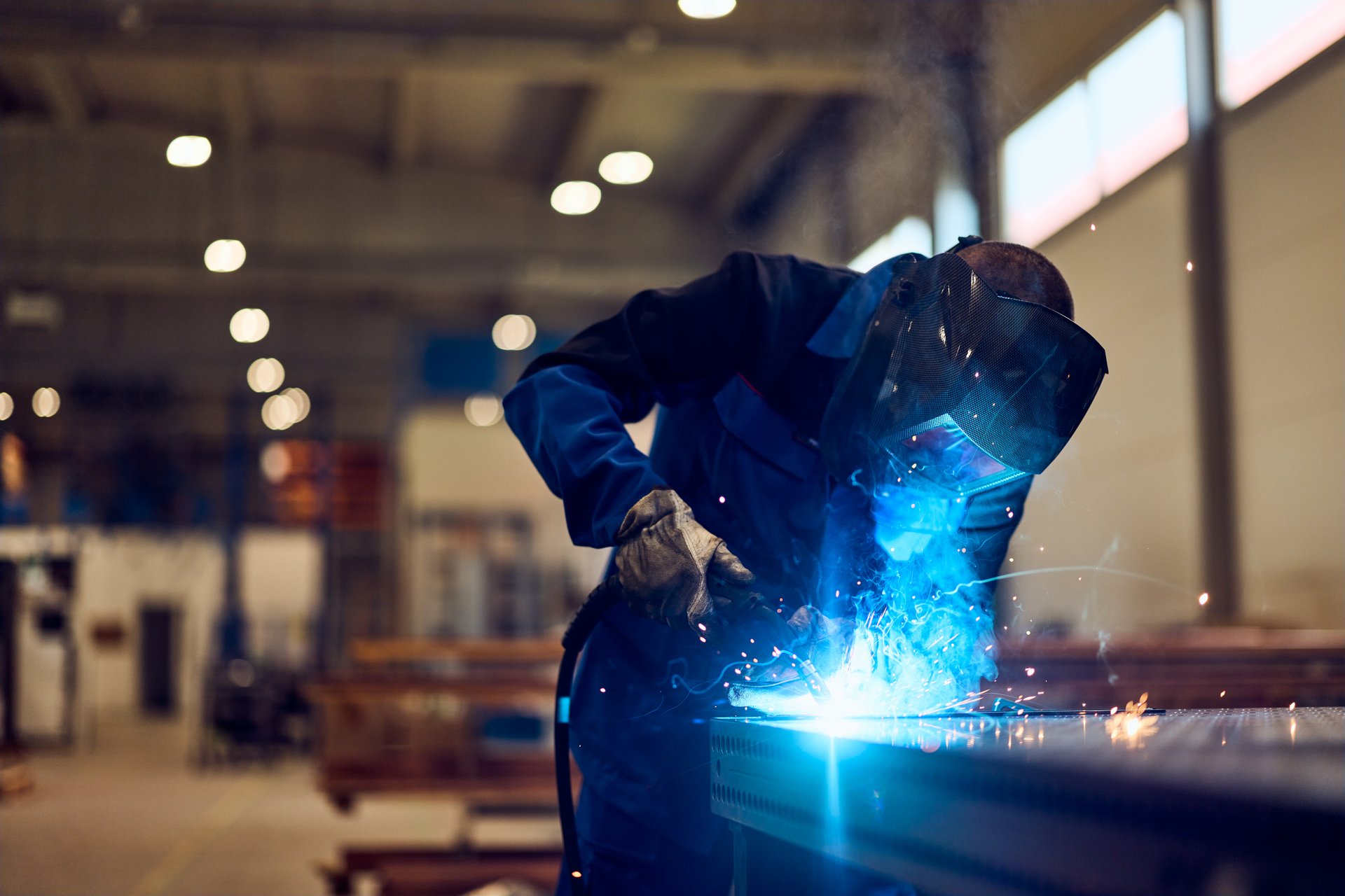 Man working in a factory operating welding machinery, with sparks and professional attire.