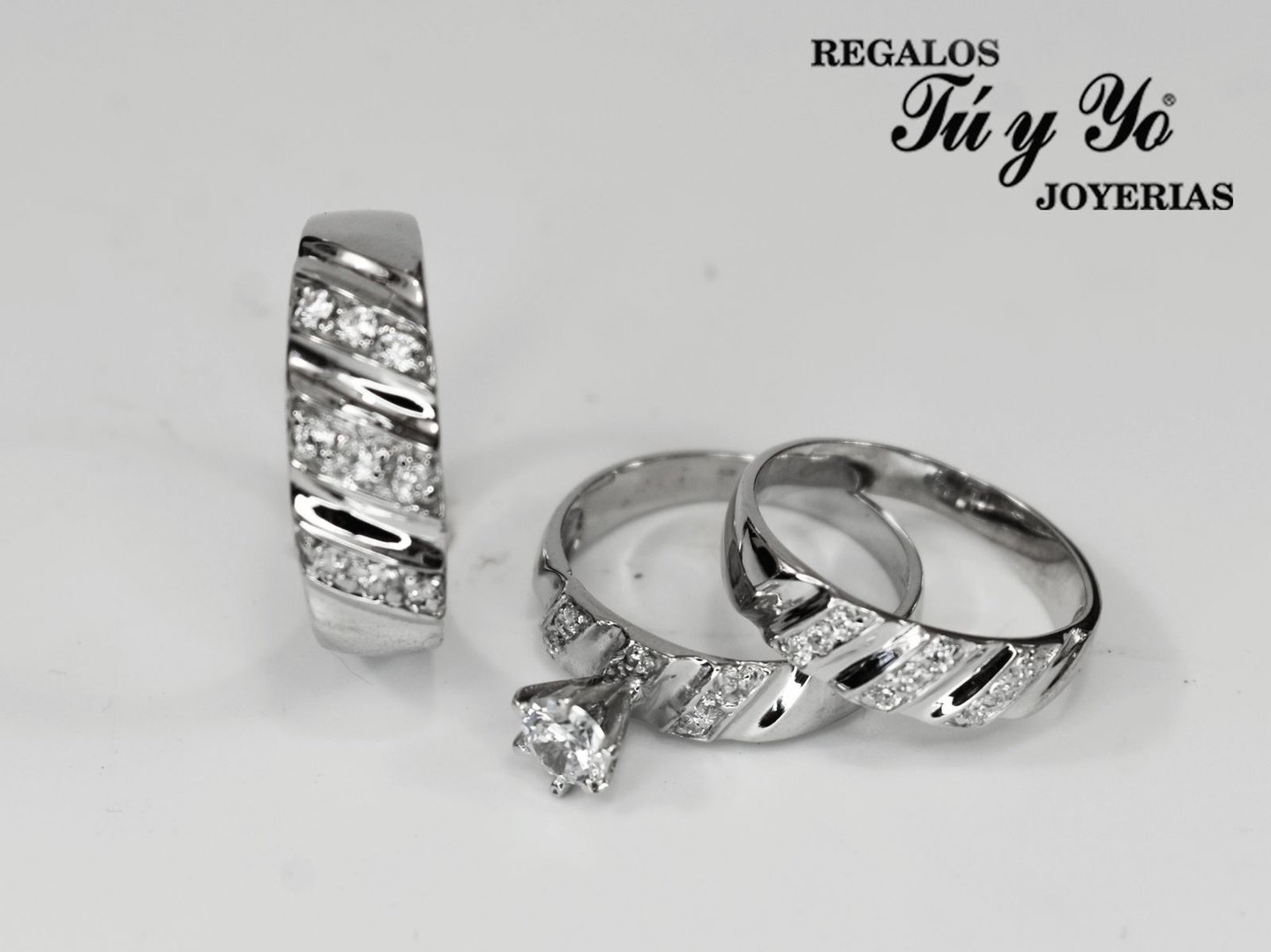 Three silver rings with diagonal grooves and embedded diamonds, featuring a solitaire diamond, displayed on a white surface.
