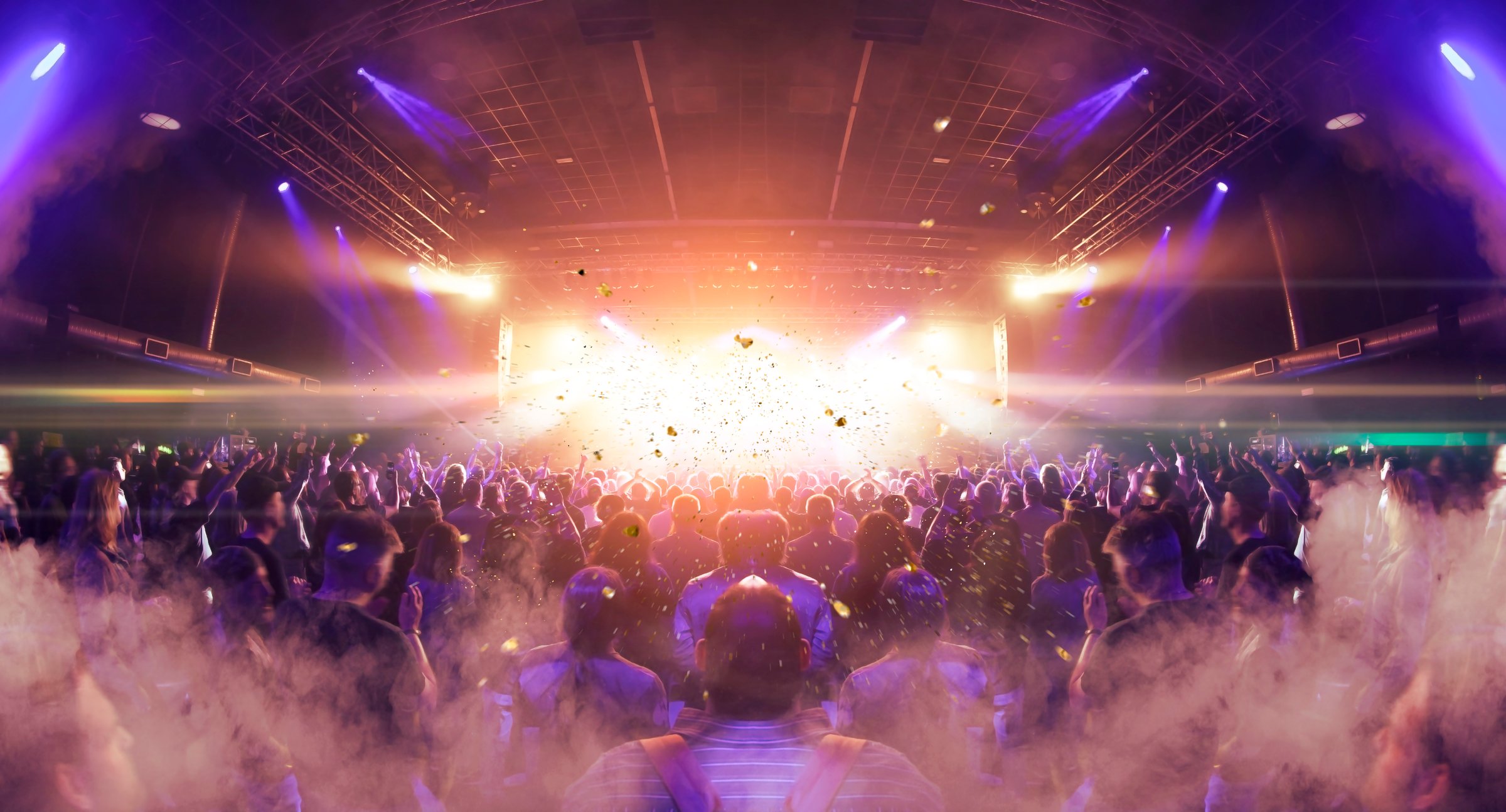 Image shot during a music festival. Light comes from a stage with a band show, people silhouettes are visible in front of it.