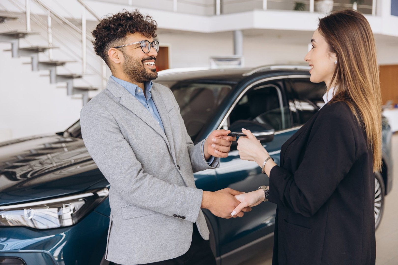 Saleswoman shaking hands and delivering car keys to a smiling customer in a car dealership, buying a new vehicle