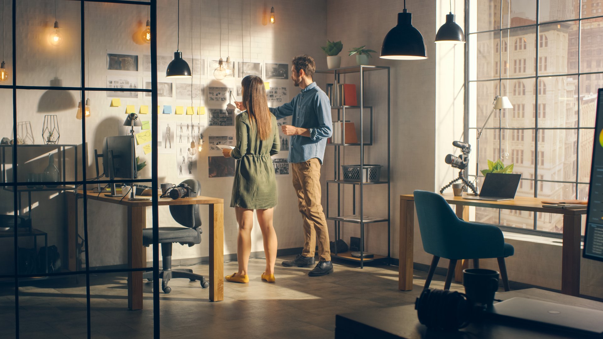 Young Creative Male and Female are Organizing a Mood Board on a Wall of Their Cool Office Loft. Pictures Represent Future Motion Video. Colleagues are Working and Discussing the Project. Sunny Day.