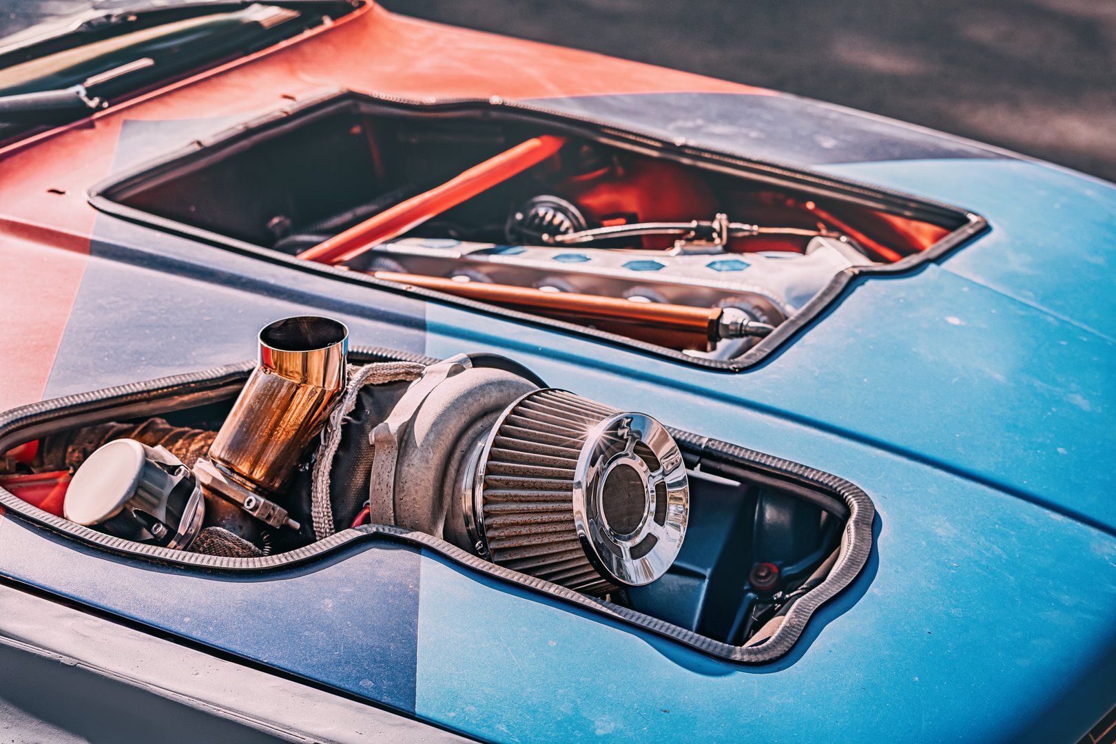 Close up of a racing car engine, a large turbocharger and air filter protruding from the hood, symbolizing power and speed