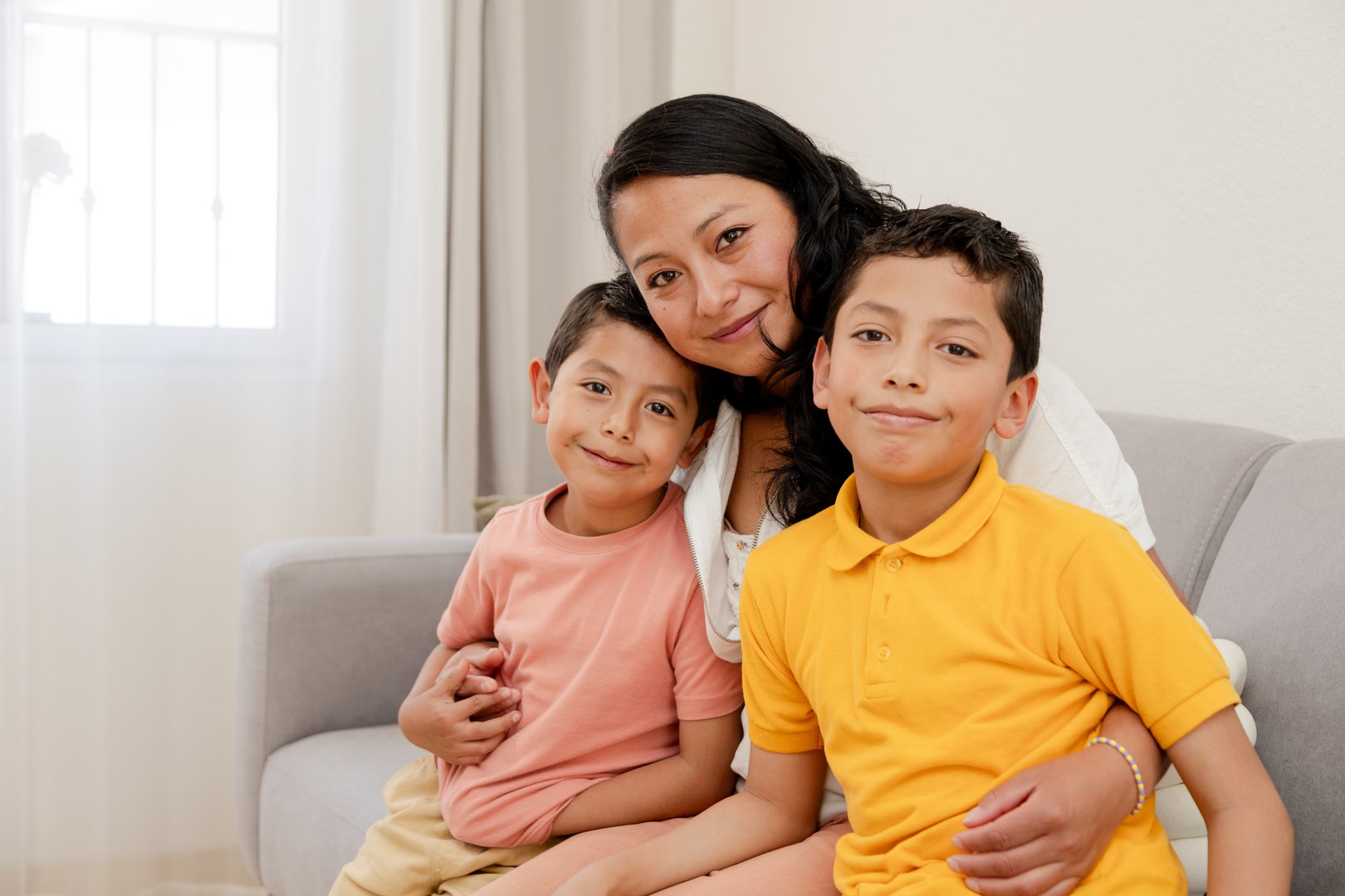 Portrait of mom and children at home-mom hugging hers two children in the living room of her house-single mother with her children-happy little family-Hispanic family