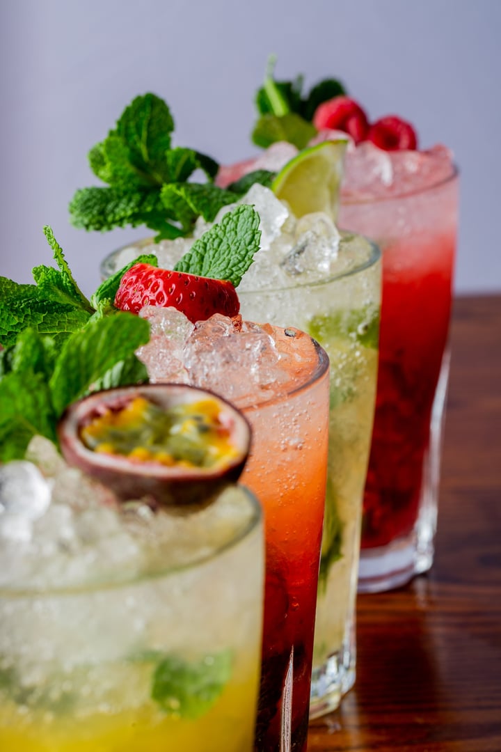 A vertical closeup of a variety of mojitos in a row on wooden table