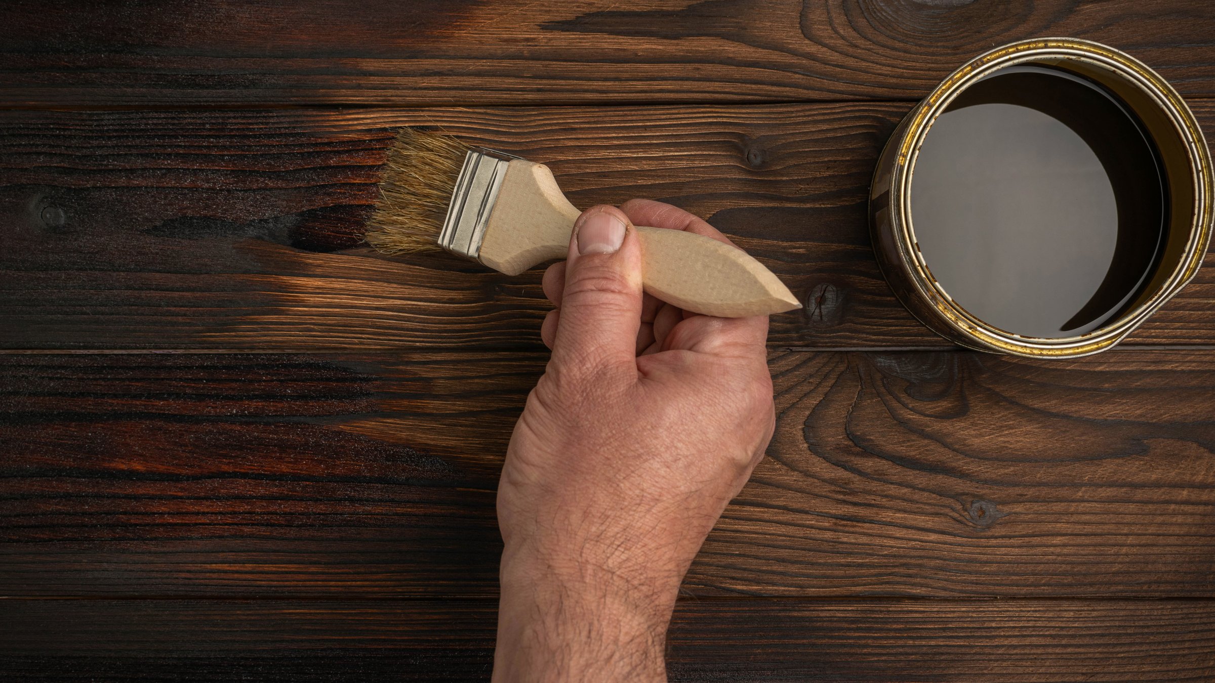 Hand Applying Wood Stain on Wooden Surface with Brush Creating Dark Finish