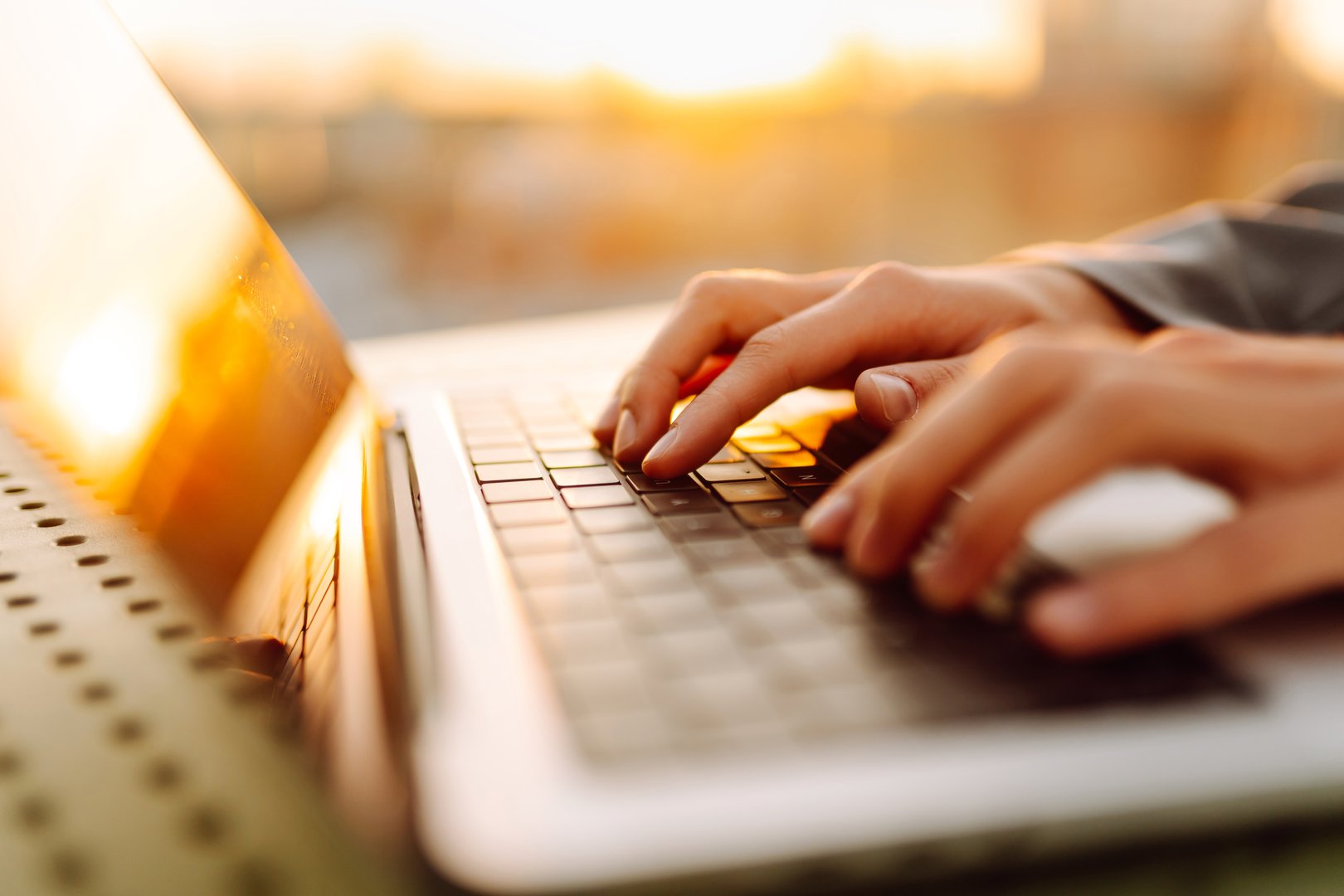 Close-up of hands typing on a laptop. Young female hands working on a laptop in the rays of the sunset. Freelance, technology concept.