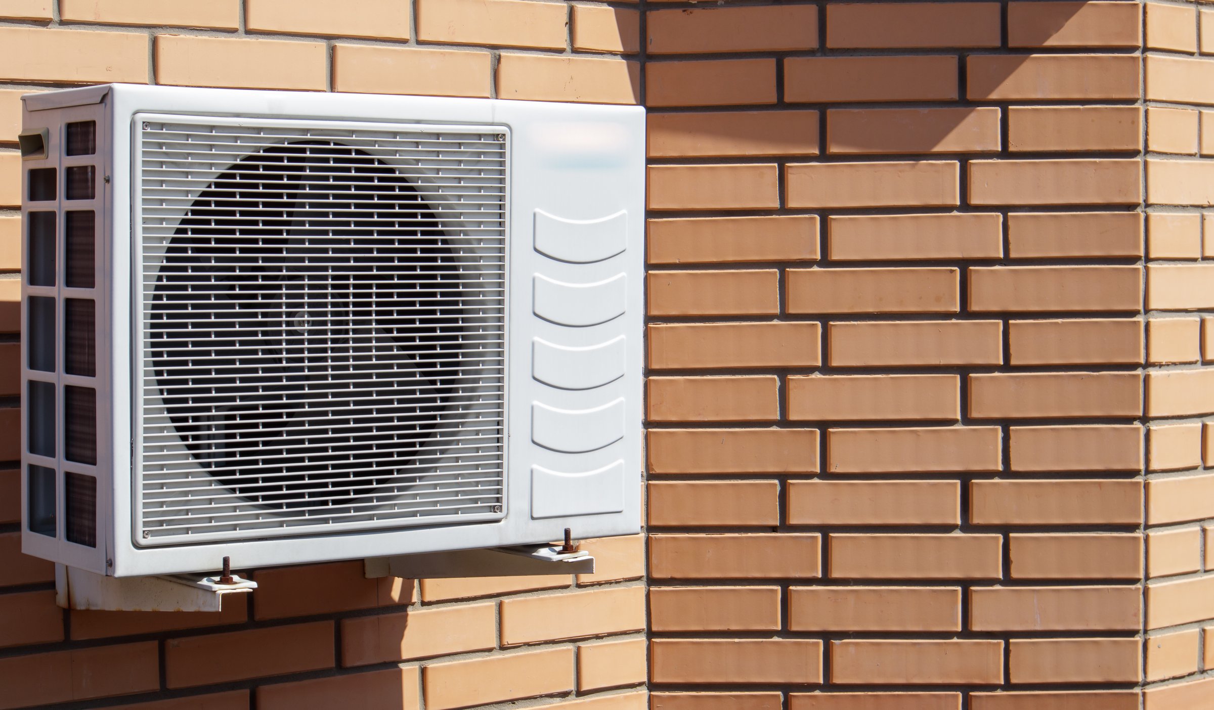 Close-up shot of a modern climate control unit against the background of a brick wall of the facade of a house outside. Air conditioner on the wall with space for text. Air compressor