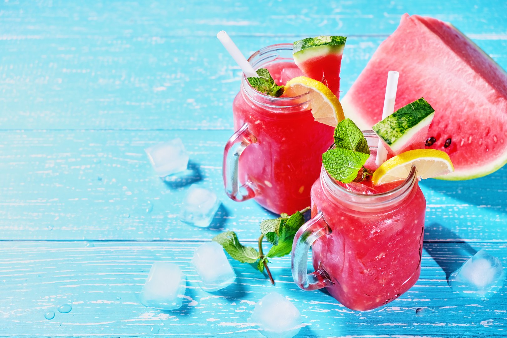 Watermelon summer cocktail with ice and mint leaves. Cold refreshment organic non-alcohol drink on blue wooden background with copy space.