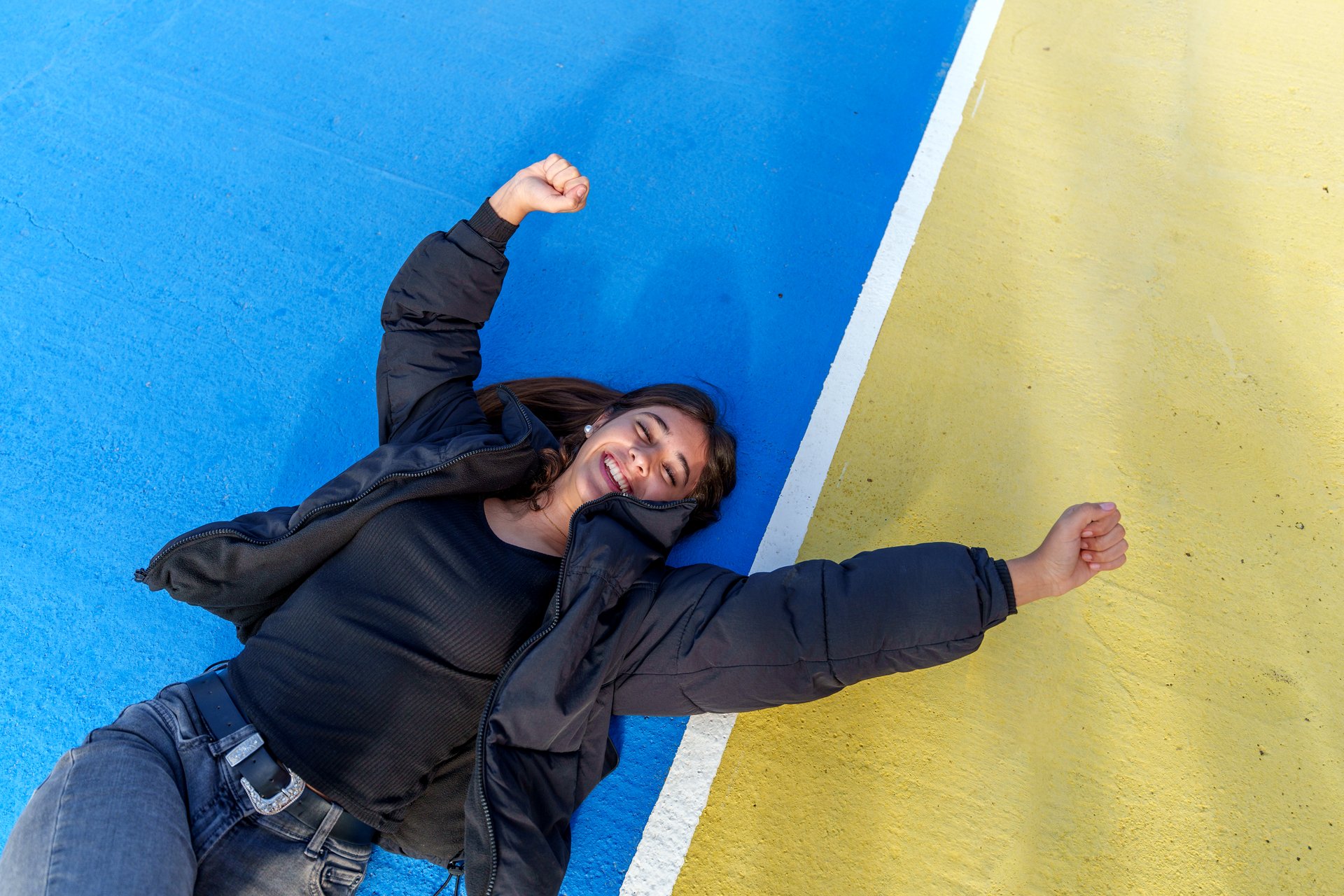 Carefree young woman lying on the ground of a basketball court with arms raised, enjoying freedom and happiness