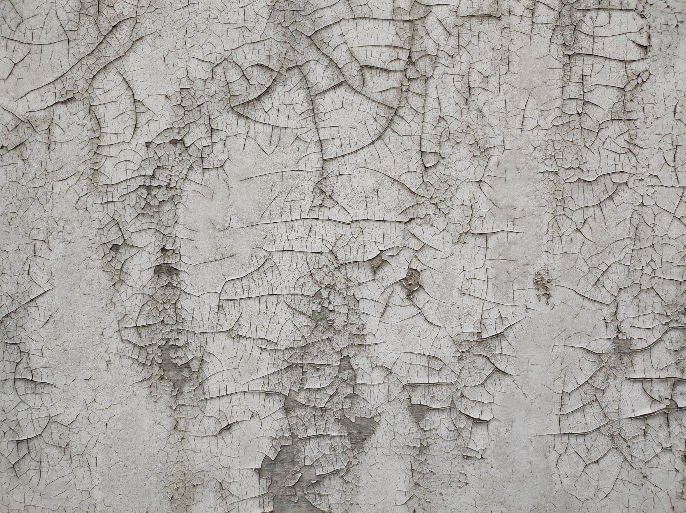 Cracked Wall Texture. A close-up view of a cracked wall, showcasing intricate patterns formed by peeling paint. The neutral tones emphasize the aged and weathered surface.
