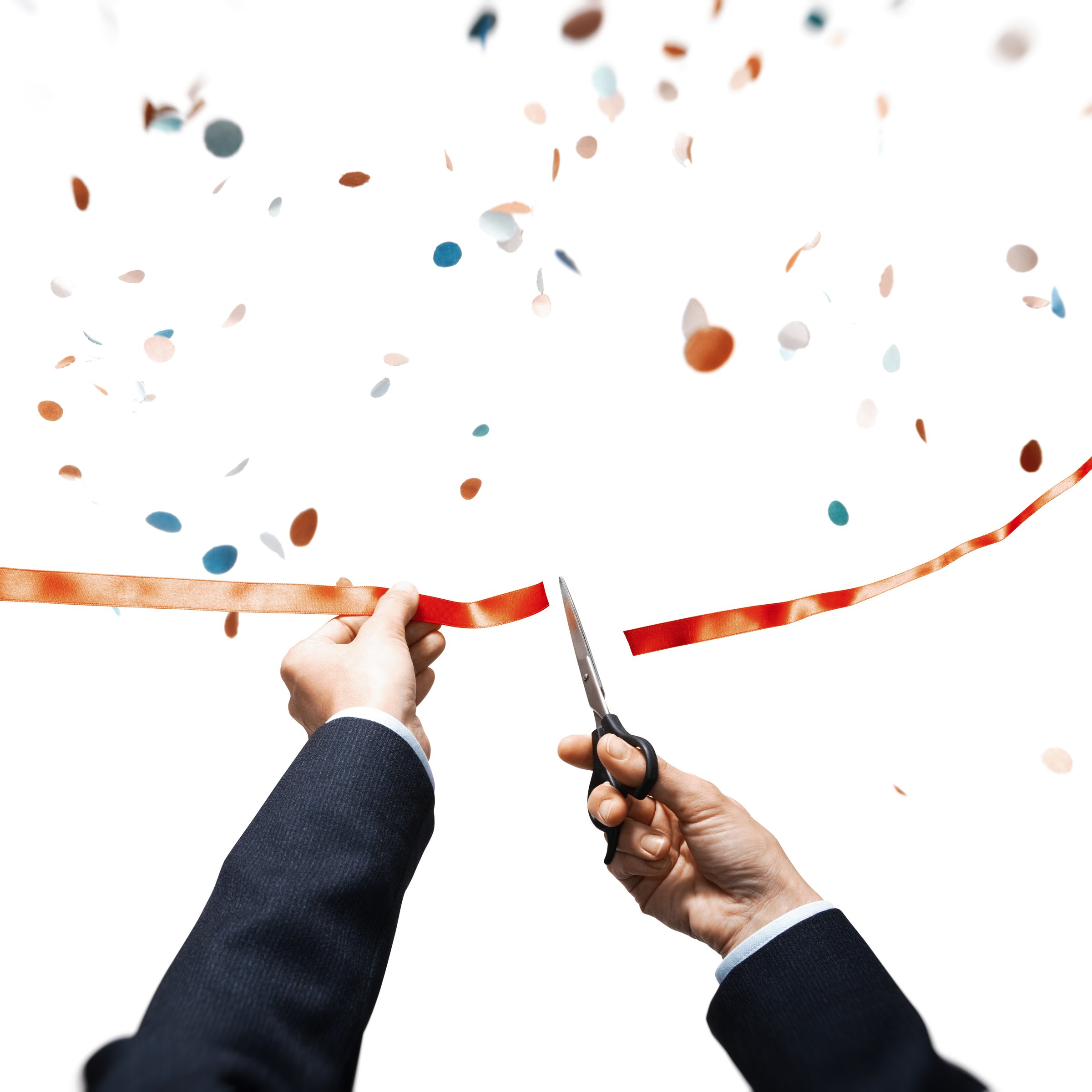 Scissors in hands cuts the red satin ribbon and colorful paper confetti is falling.