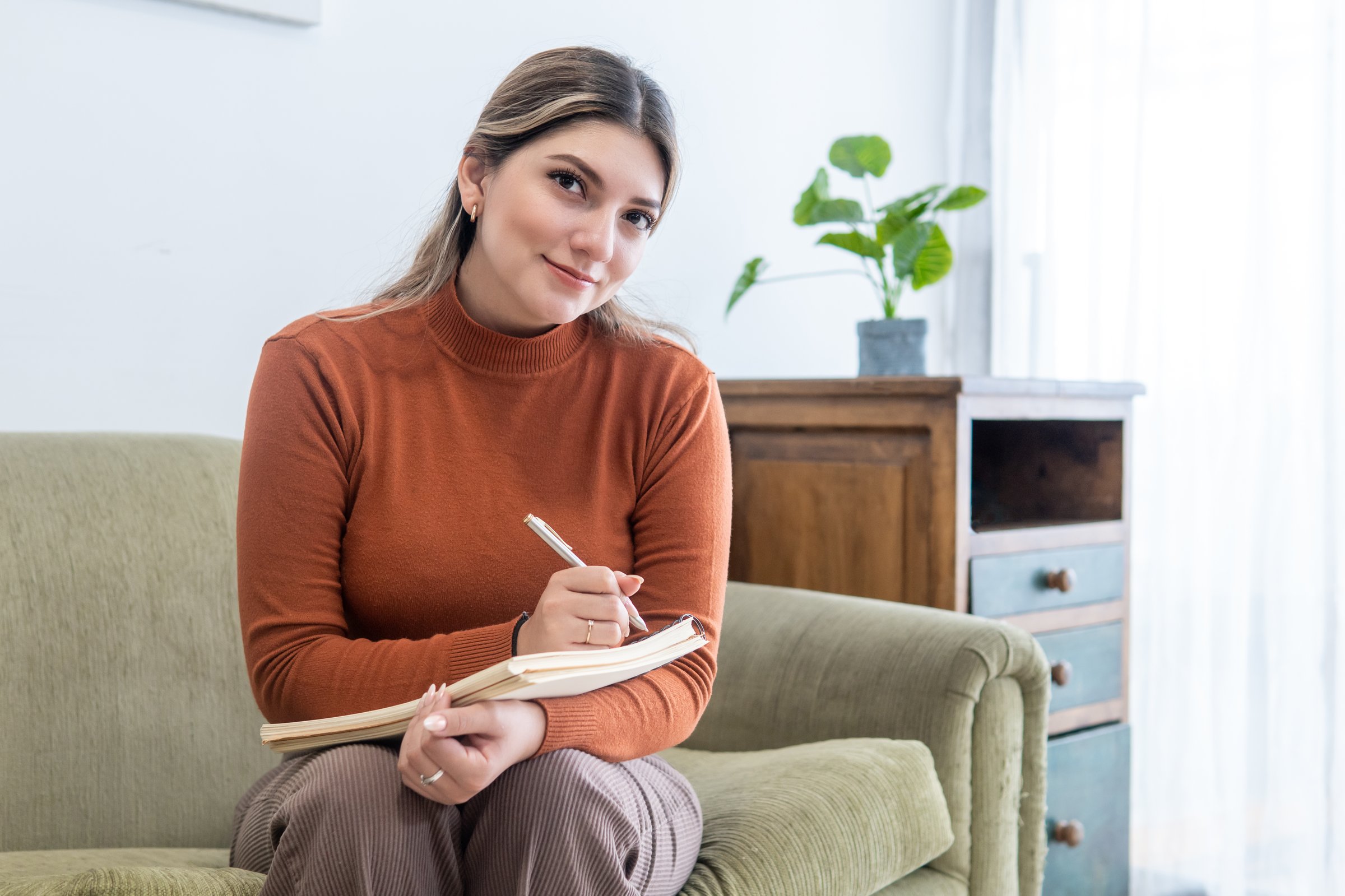 Young female psychologist looking at camera with her notebook and a pen in her office