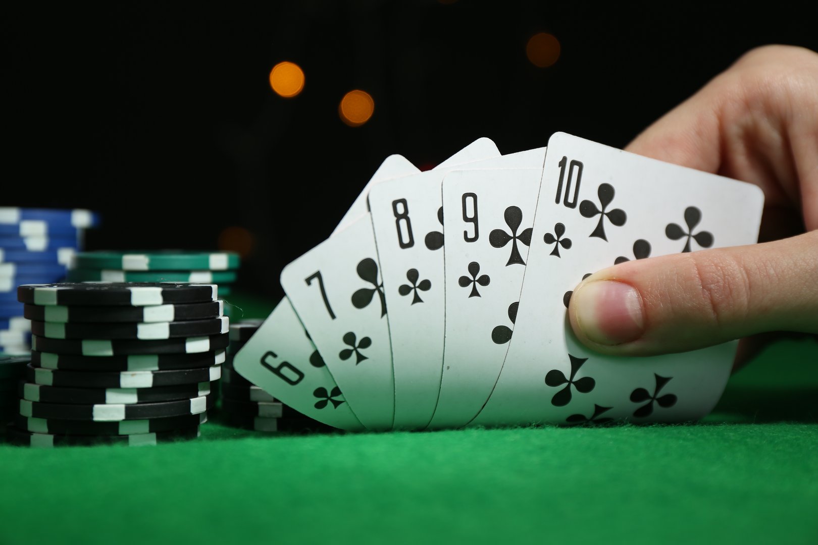 Poker game. Woman with playing cards and chips at green table, closeup