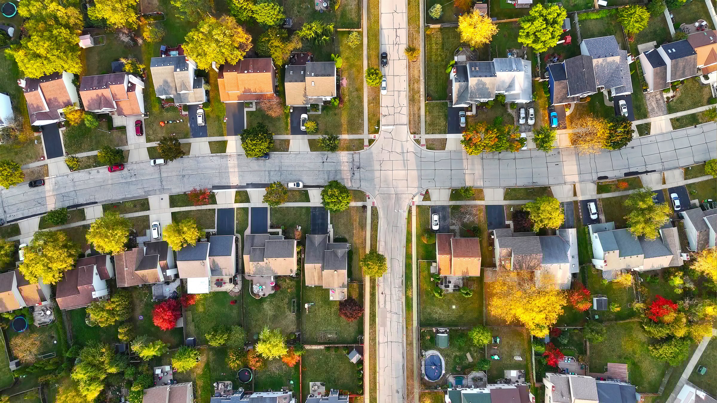 Aerial View of Suburban Neighborhood in Autumn. Top-down aerial shot of a suburban neighborhood with neatly arranged houses, driveways, and colorful autumn trees lining the streets