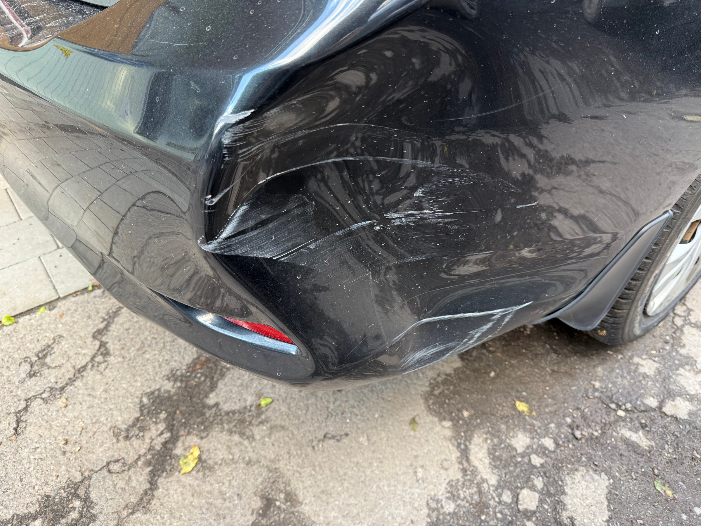 Close-up view of a damaged and scratched black car bumper after a minor accident, showing a significant dent and scrapes on the paintwork requiring repair and insurance claim
