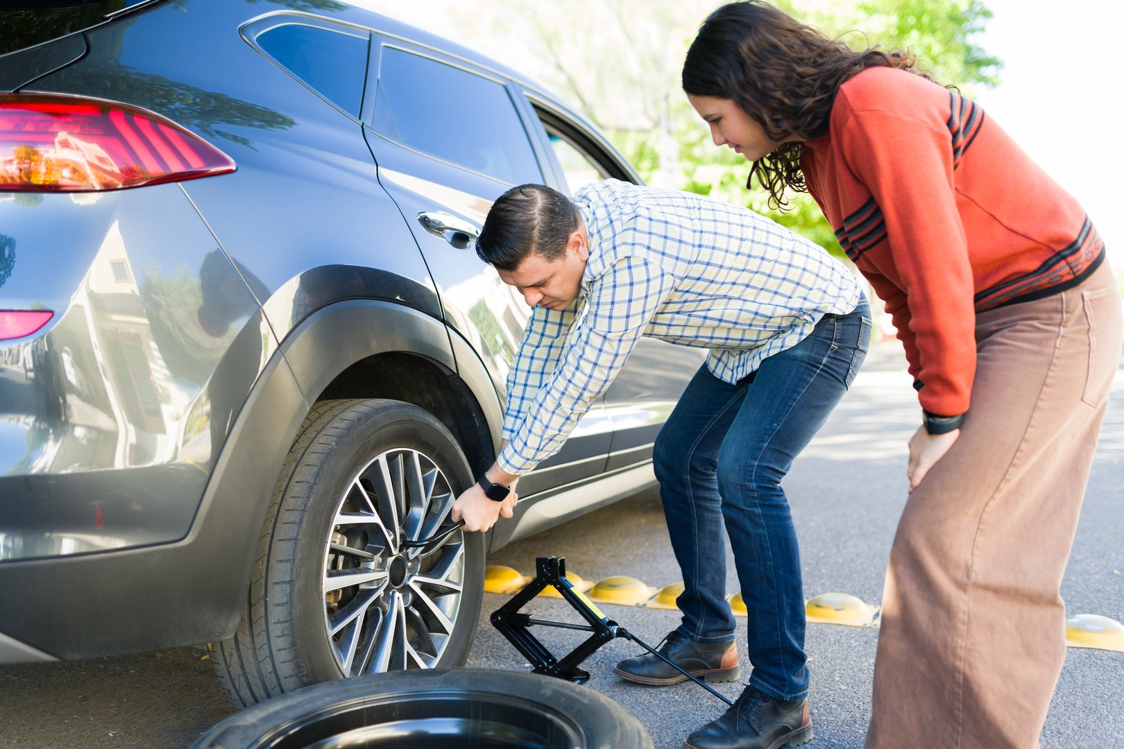 Father teaching his teenage daughter how to change a flat tire, working together on roadside maintenance