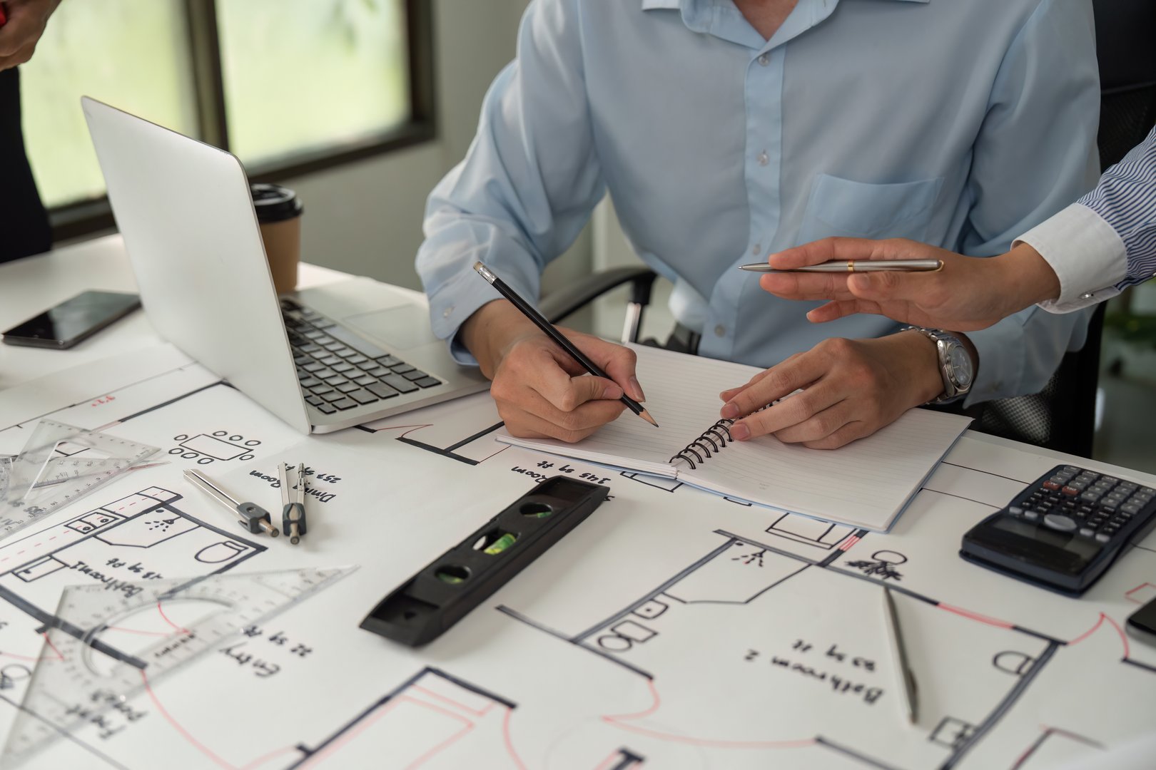 An architect meticulously drafting detailed plans while collaborating with colleagues to ensure accuracy and alignment during the design phase.