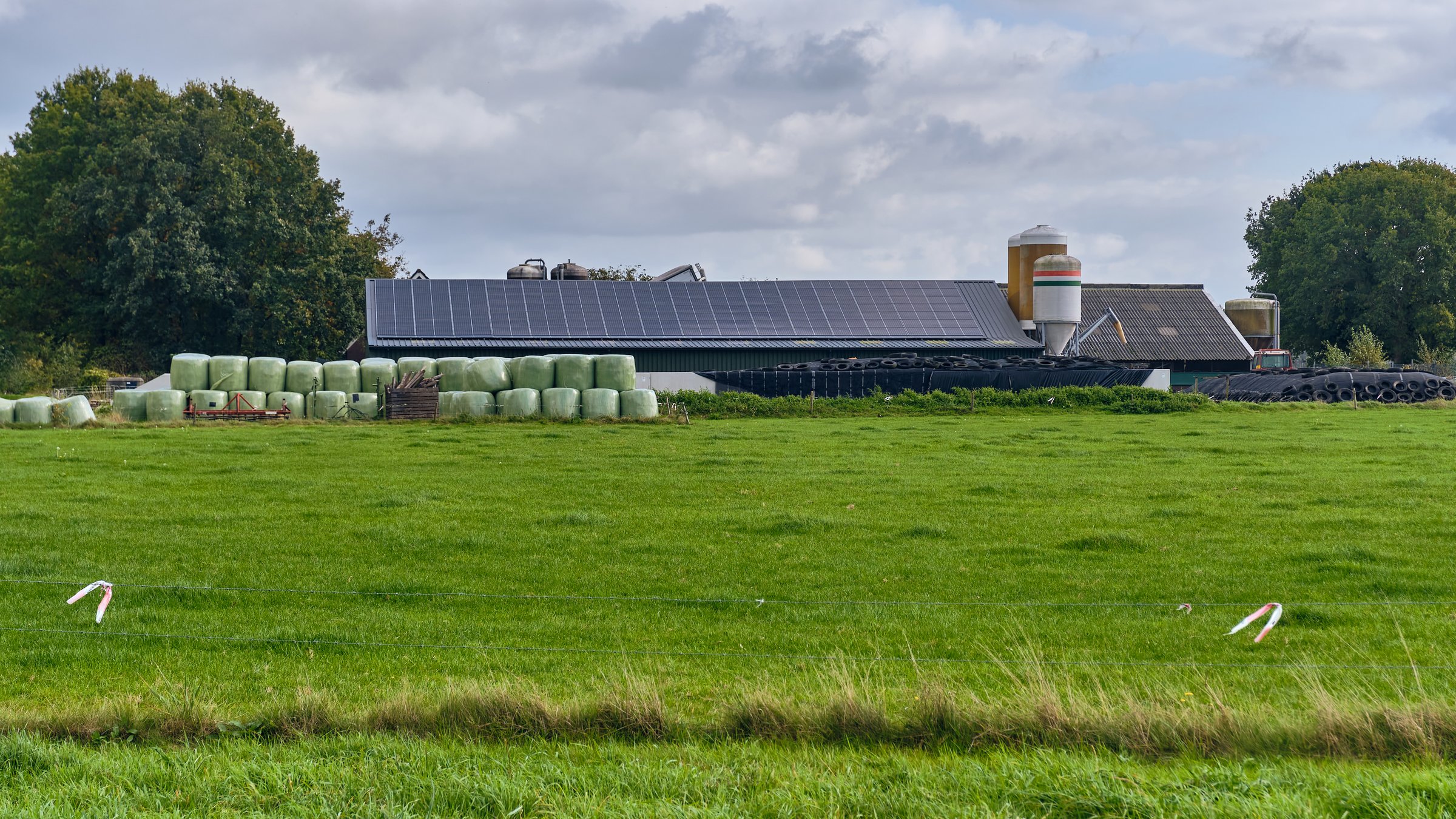 Langelo, Netherlands ; October 10, 2025: Sustainable Dutch farm with solar panel roof, silos and hay bales in rural landscape showing renewable energy and modern agriculture practices.