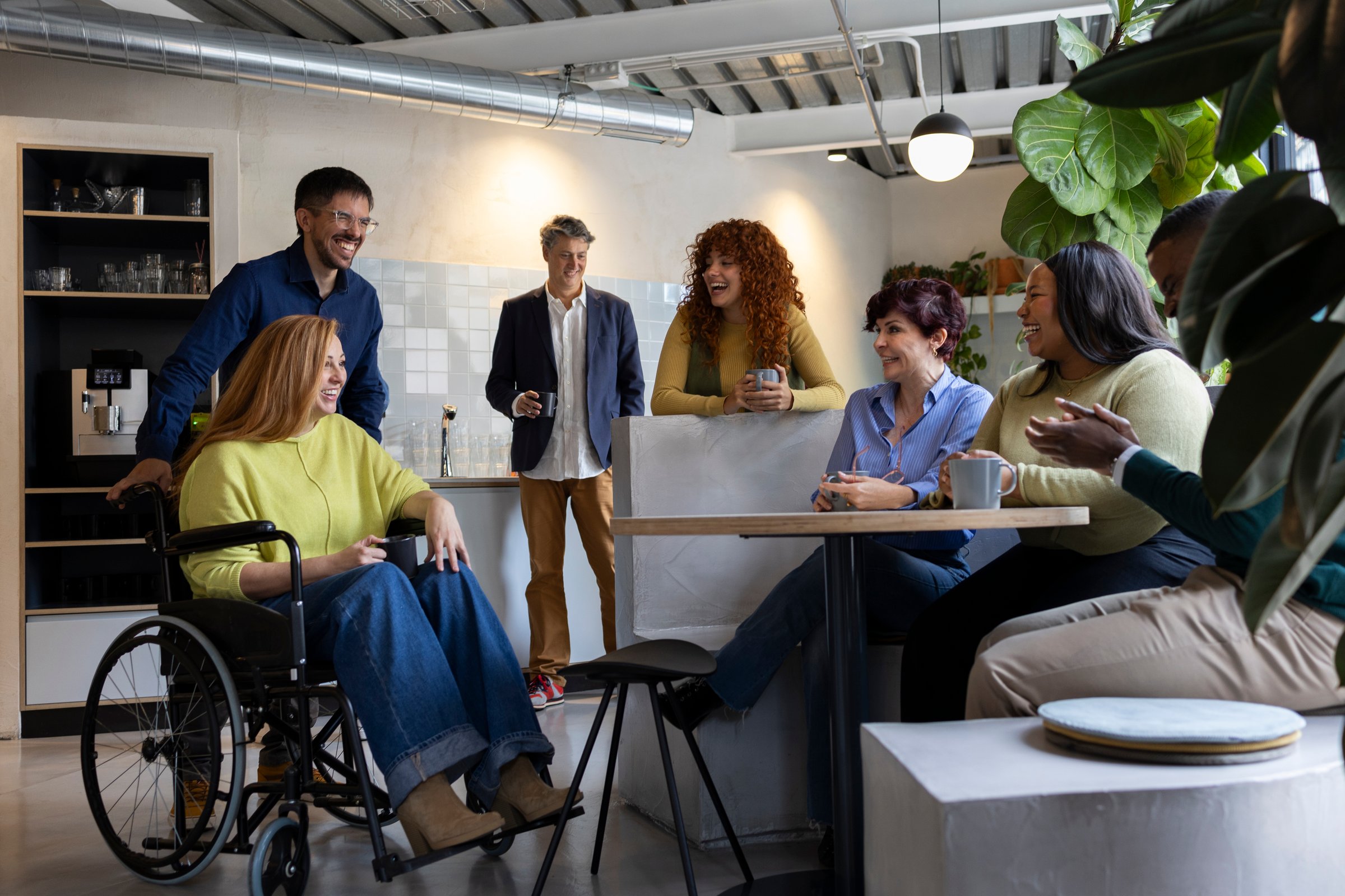 Coworkers socializing and laughing during a coffee break in an inclusive and accessible office environment