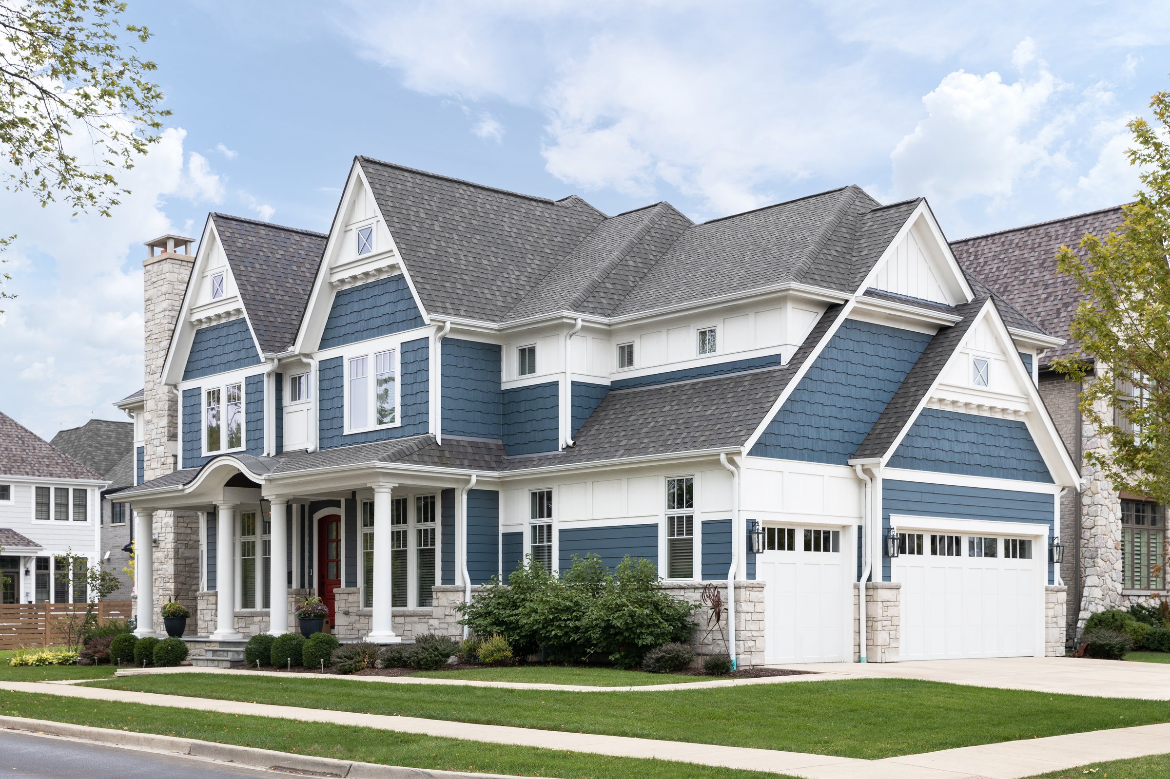 Barrington, IL, USA - October 5, 2021: A luxury, blue modern farmhouse with a covered porch, three car garage, and a stone chimney.