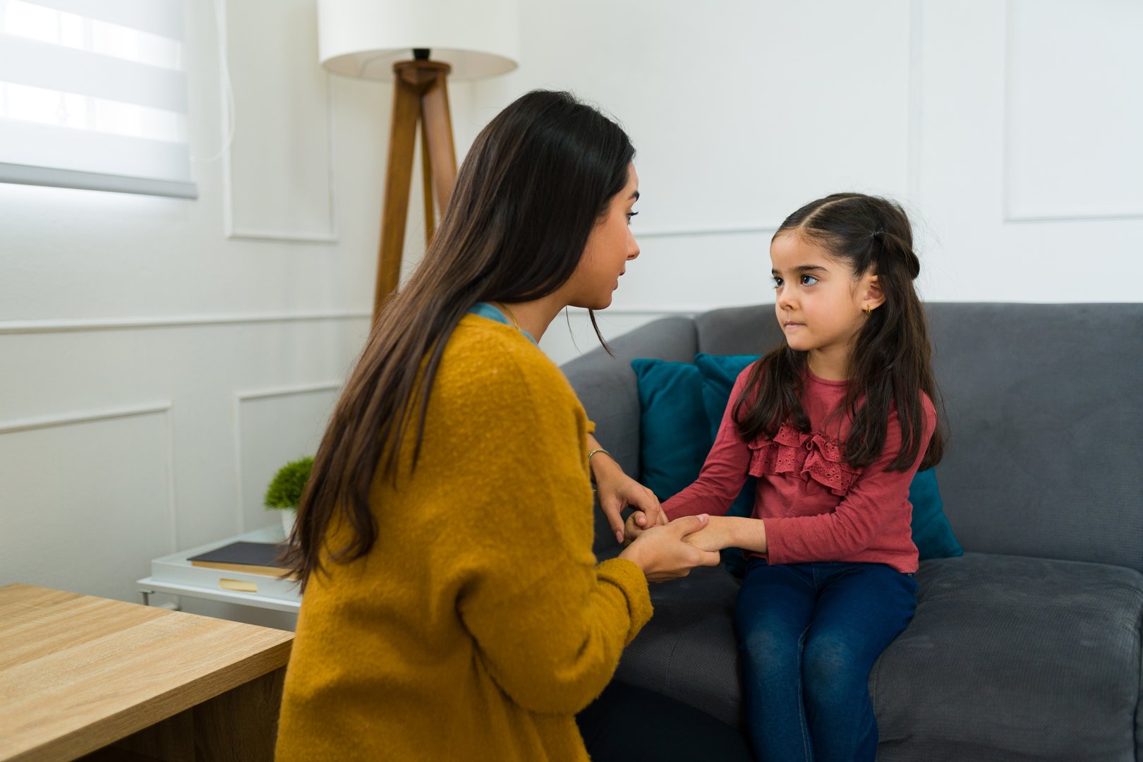 Concerned loving mother talking to her young daughter about divorce and child custody while sitting on the sofa