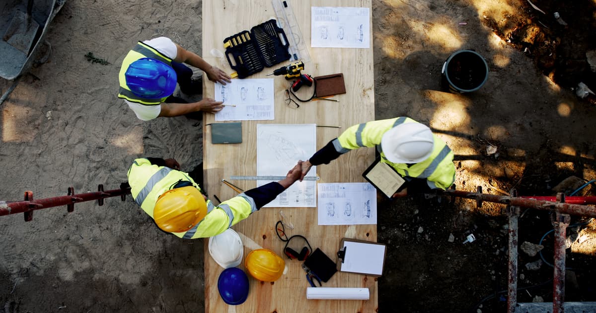 Blueprint, architecture and men at table shaking hands for collaboration, agreement and inspection from above. Construction, building team and contractor on site with floor plan, handshake and deal
