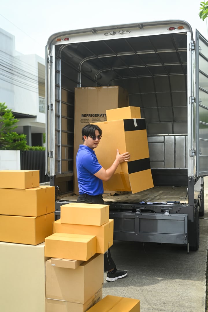 Delivery man in uniform unloading cardboard boxes from from van. Moving service and transportation concept.