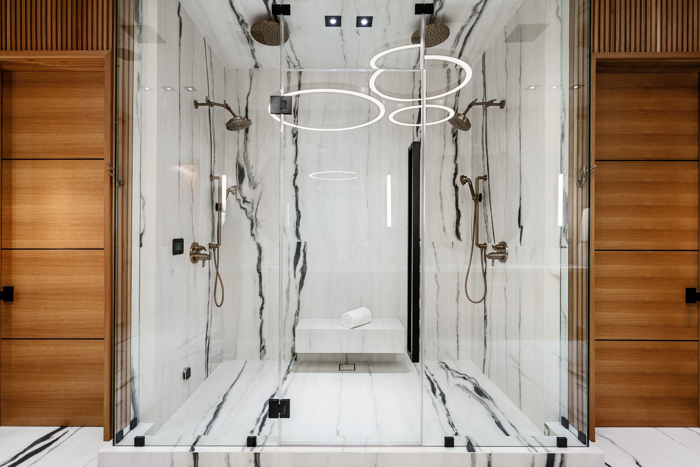 Luxurious modern bathroom with marble walls, glass shower enclosure, and wooden accents.