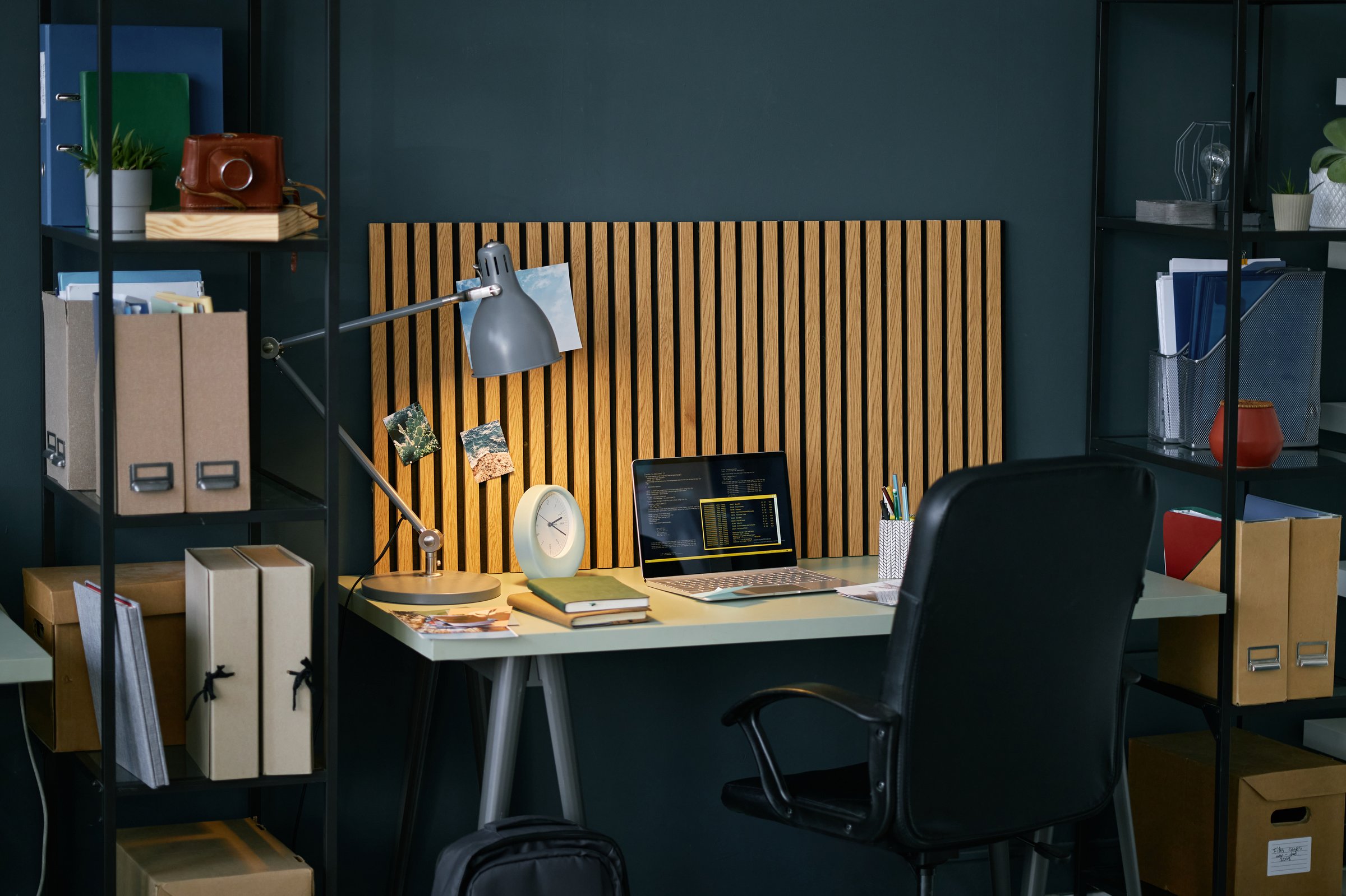 Neatly organized home office featuring wooden desk with computer setup, book, and potted plant on top. Vertical slat accent backdrop adds a touch of modernity