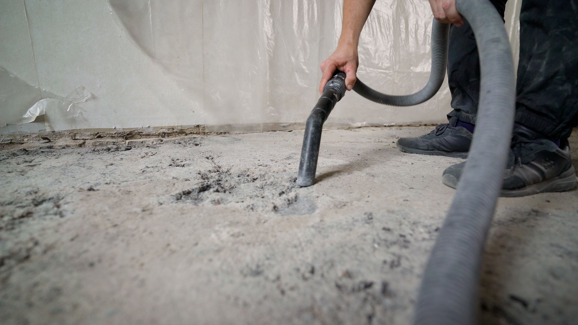 Construction worker using a powerful industrial vacuum cleaner to remove dust and debris from a concrete floor during renovation work