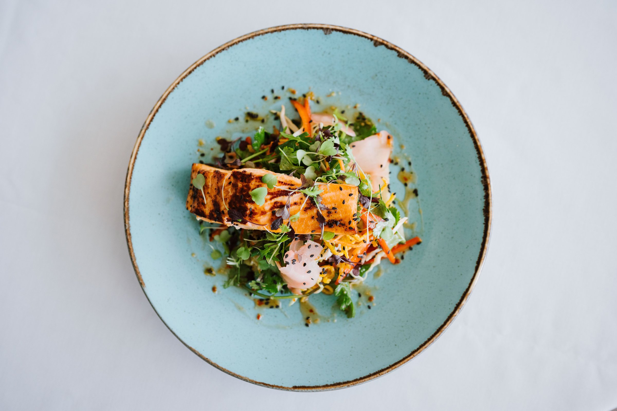 A gourmet dish of grilled salmon with fresh greens and vegetables served on a blue plate.