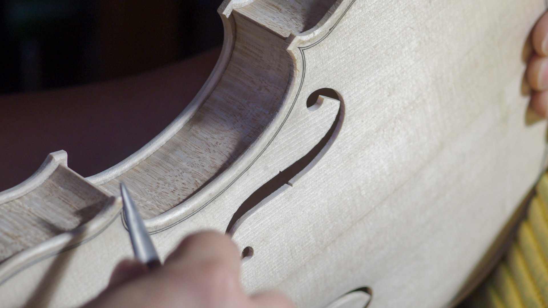 Close-up view of a luthier's hands skillfully using a gouge to carve the intricate f-hole of a violin